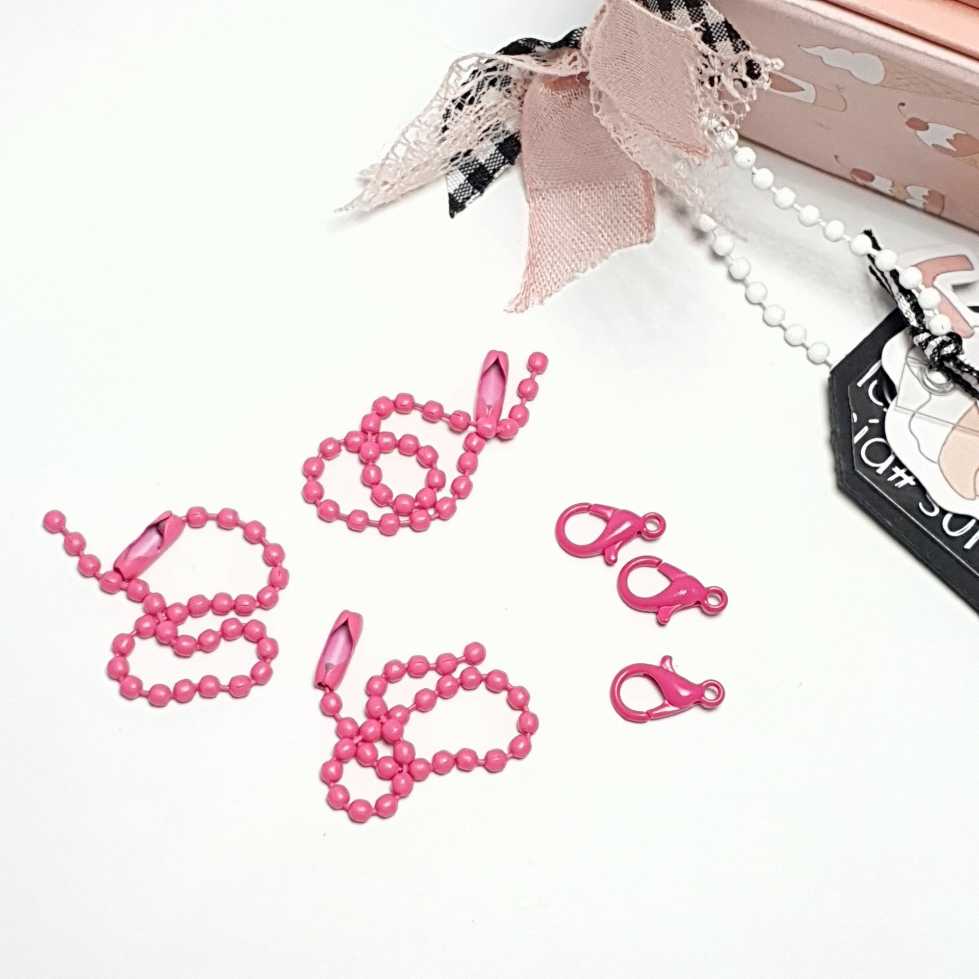 Colares rosa com contas plásticas e fechos, junto a caixa rosa decorada com fitas