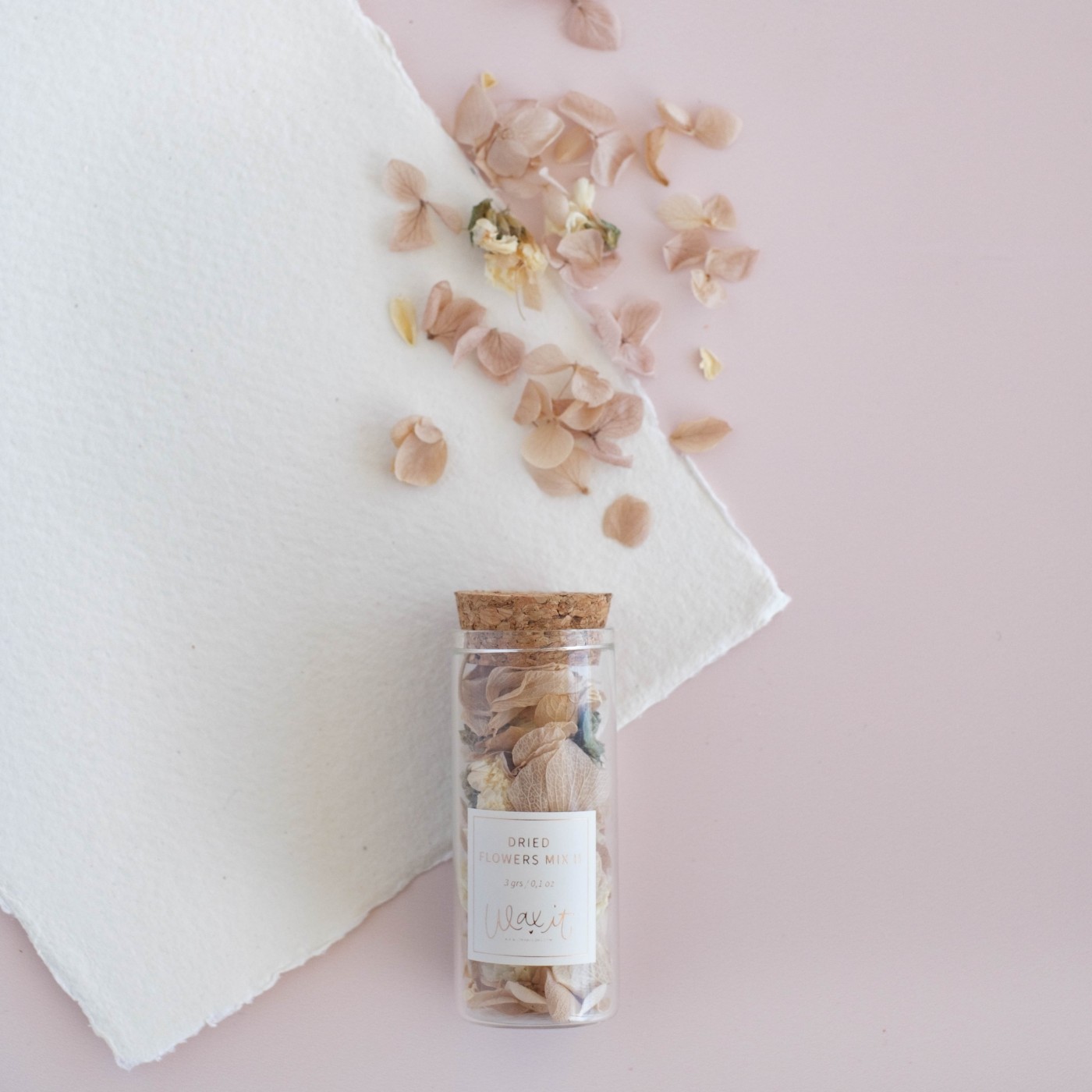 Pequeno frasco com flores secas e tampa de cortiça sobre superfície branca e fundo rosa