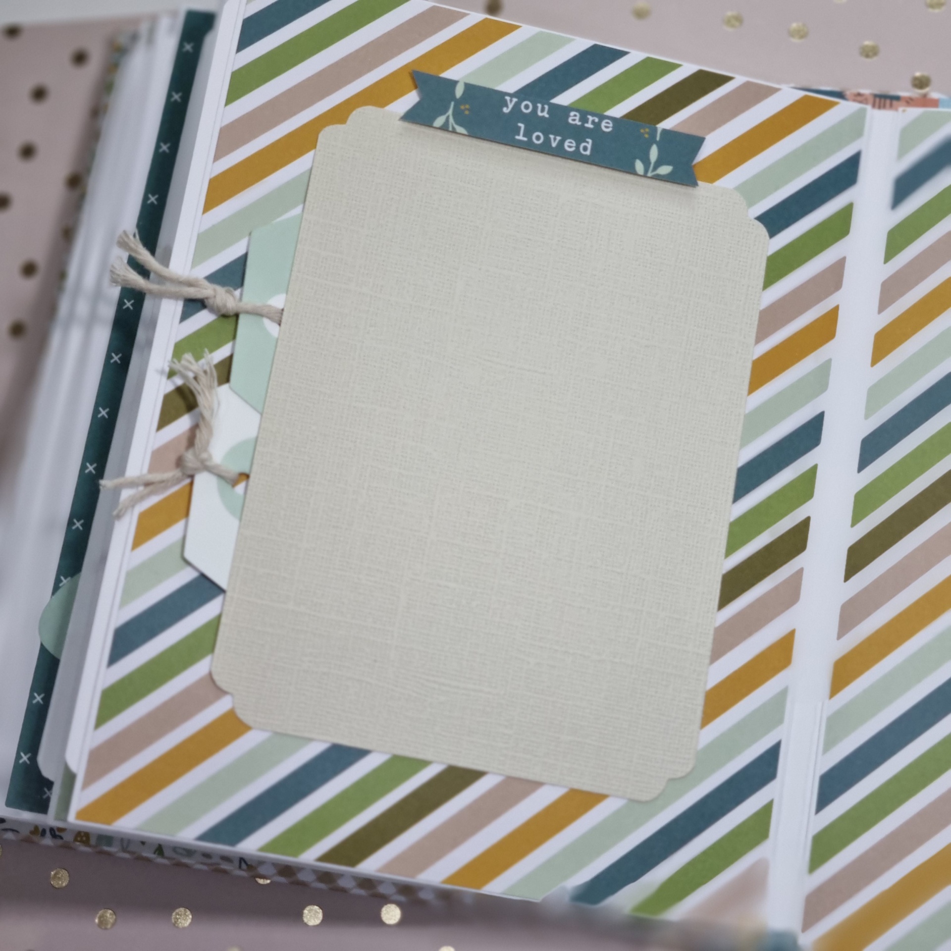 Página de álbum com fundo listrado colorido e cartão branco com etiqueta 'you are loved'