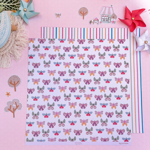 Papel decorativo com padrão de borboletas coloridas e bordas listradas sobre mesa rosa com decoração