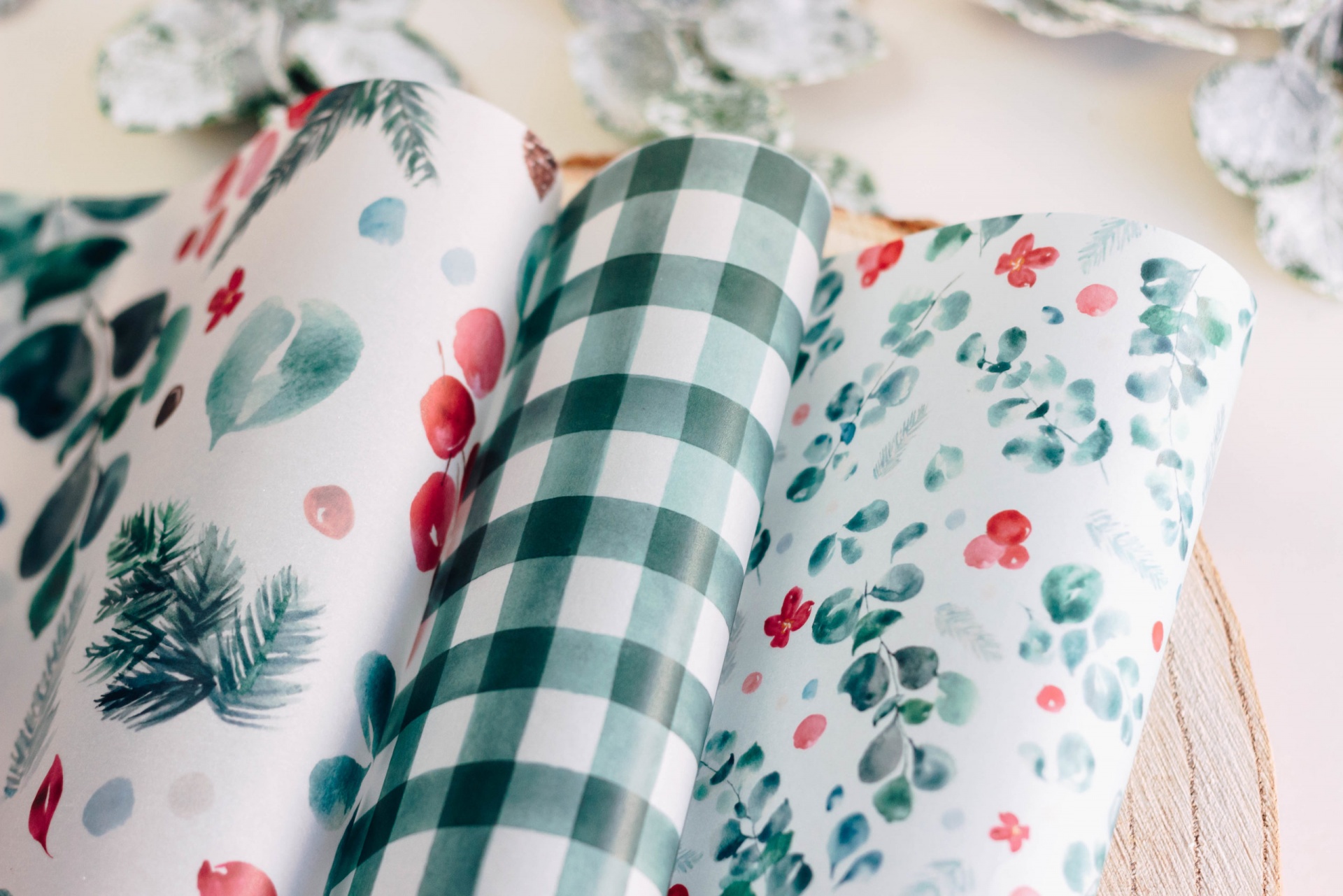 Rolos de papel de embrulho com padrões natalícios em cima de mesa de madeira