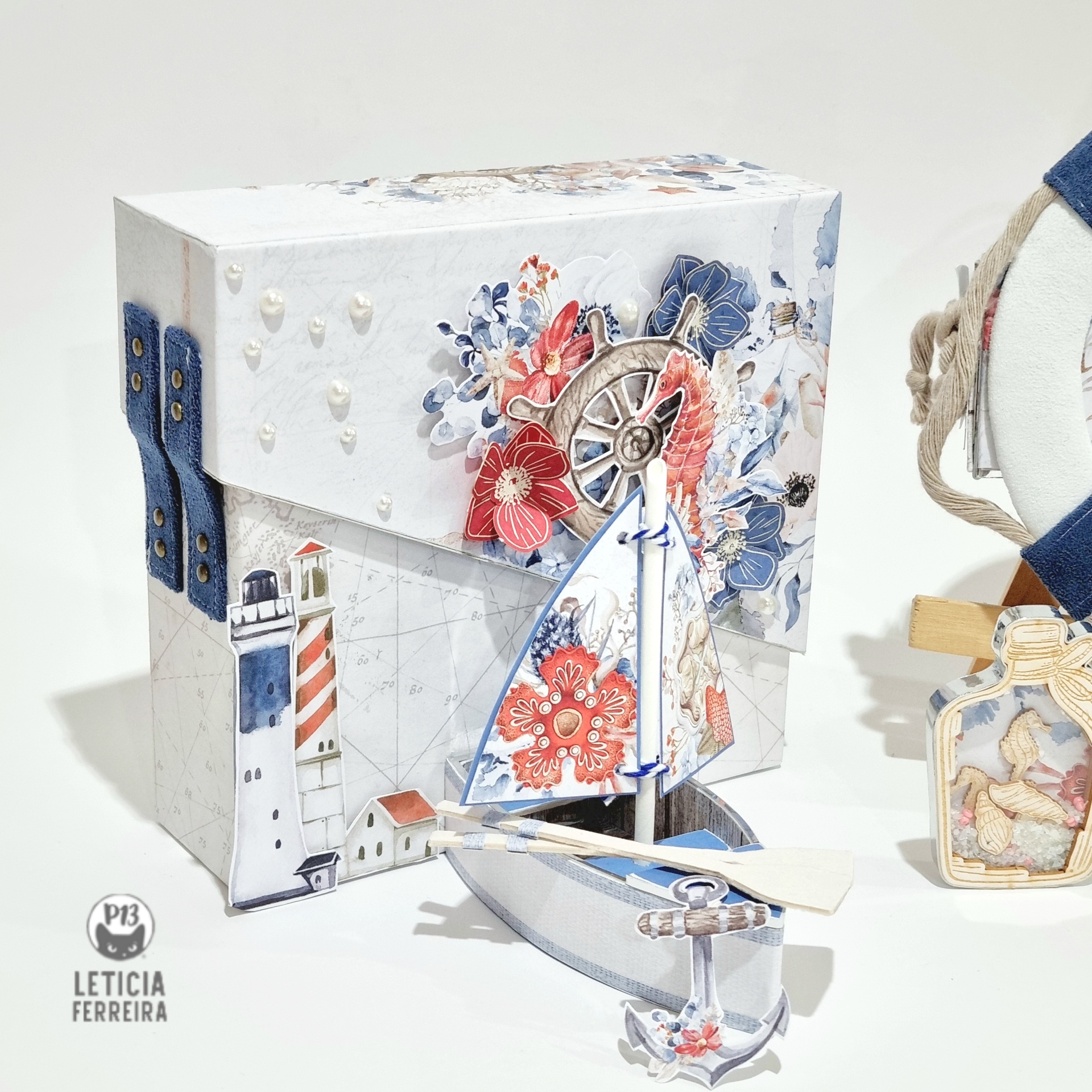 Caixa decorativa náutica com farol e flores, acompanhado por mini barco de vela decorativo