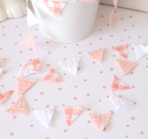 Guirlanda decorativa em triângulos de tecido rosa e branco sobre superfície com bolinhas cor-de-rosa