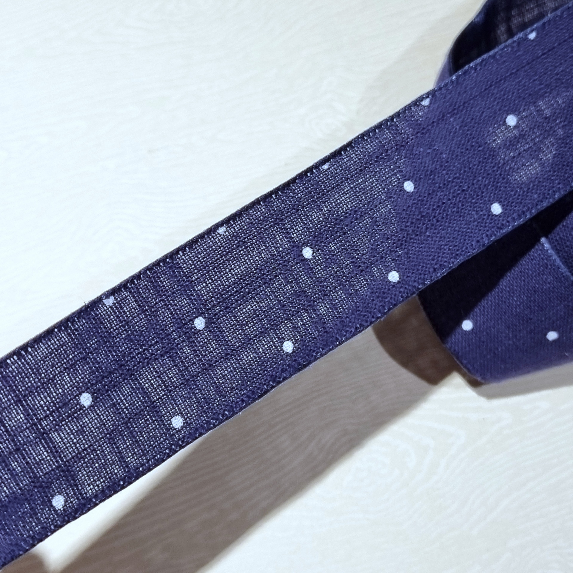 Gravata azul escura com bolinhas brancas sobre superfície clara
