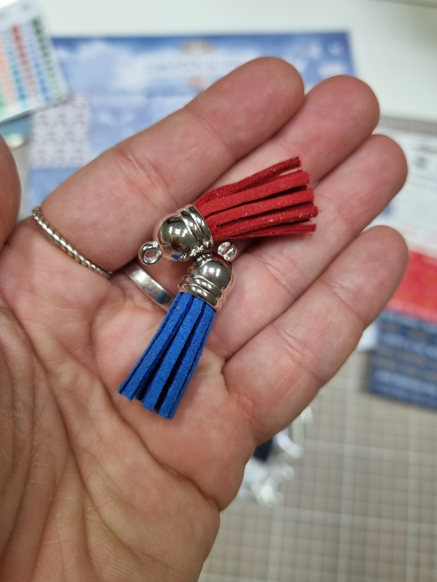 Pendentes de franjas azul e vermelha em camurça com ponteiras metálicas prateadas na mão.