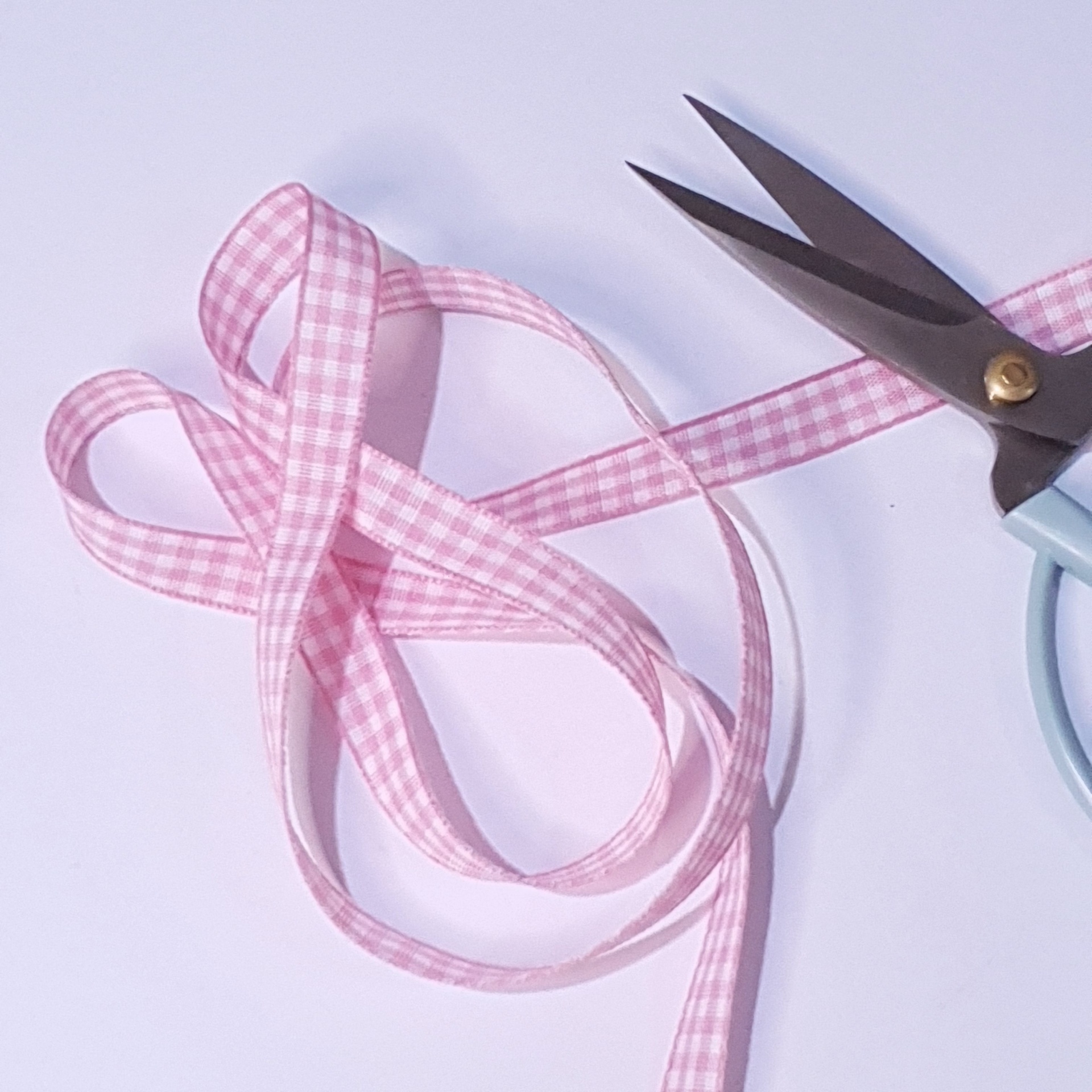 Fita rosa xadrez branca e tesoura com cabo azul claro sobre superfície branca