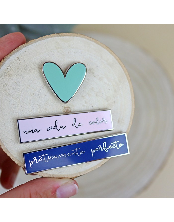 Pins em metal com esmalte azul, rosa e coração azul claro sobre base de madeira