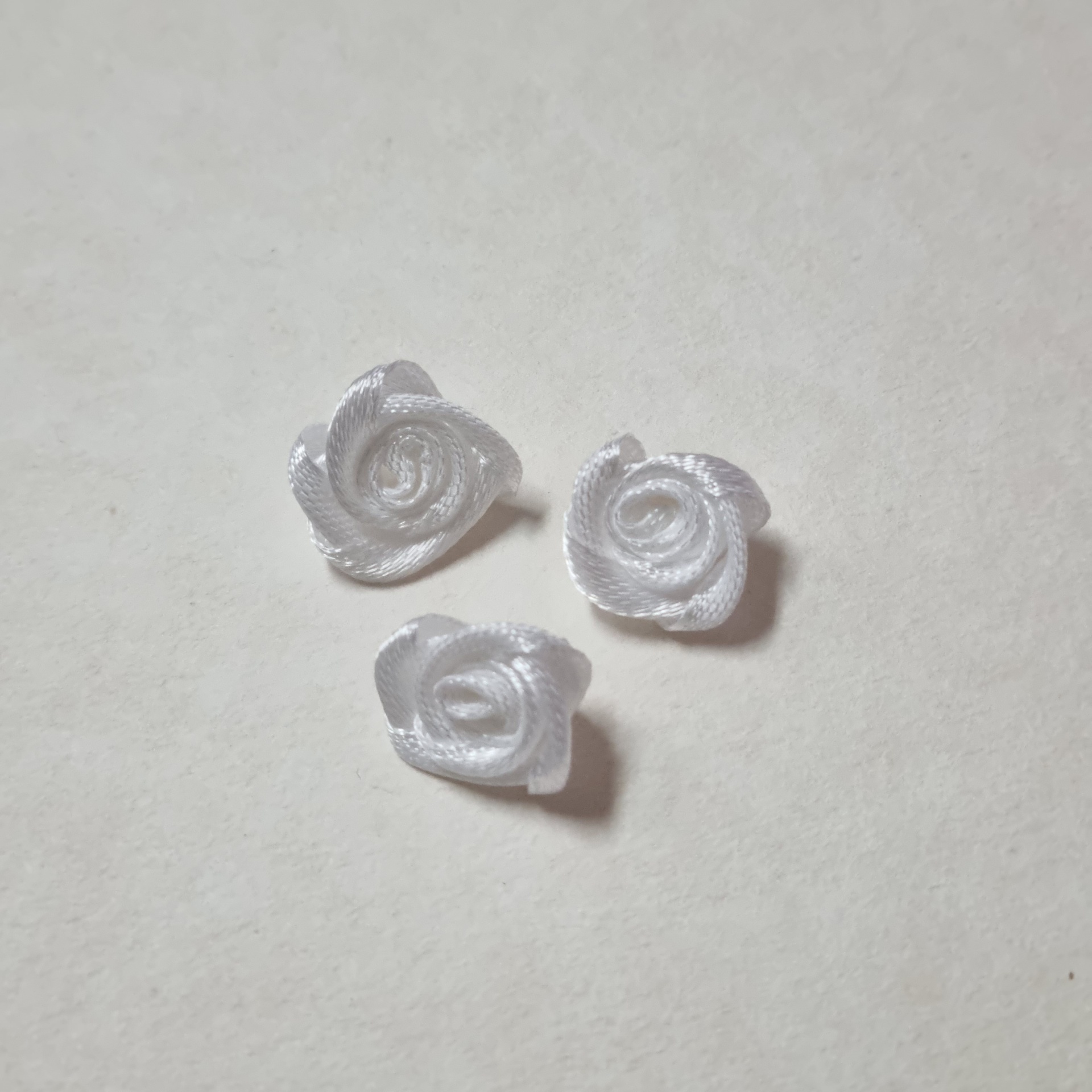 Três rosas brancas feitas de fita de cetim sobre superfície clara
