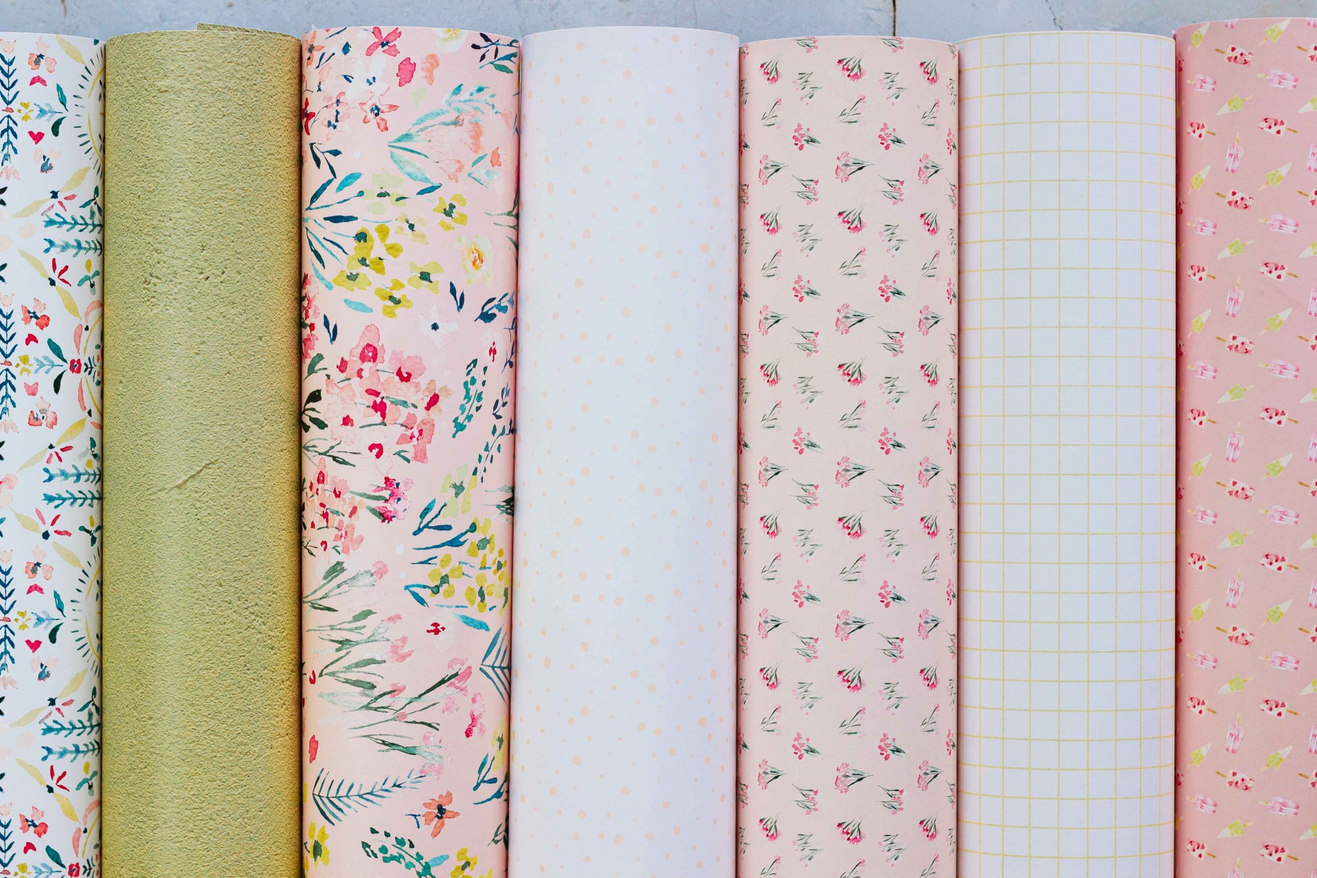 Sete rolos de tecido com diferentes padrões florais e cores pastel