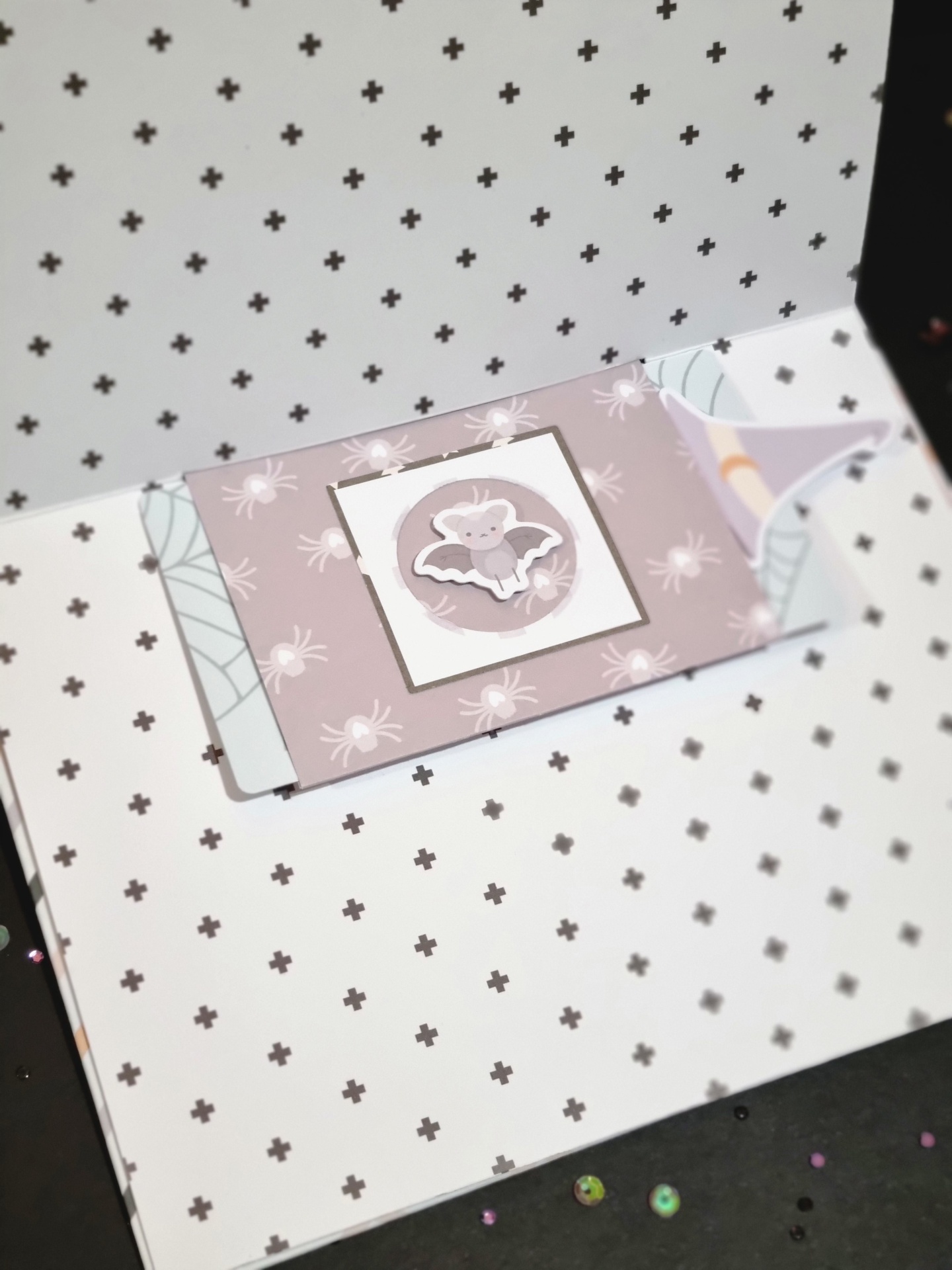 Caixa branca com padrão de cruzes pretas e cartão lilás com padrão de aranhas e morcego.