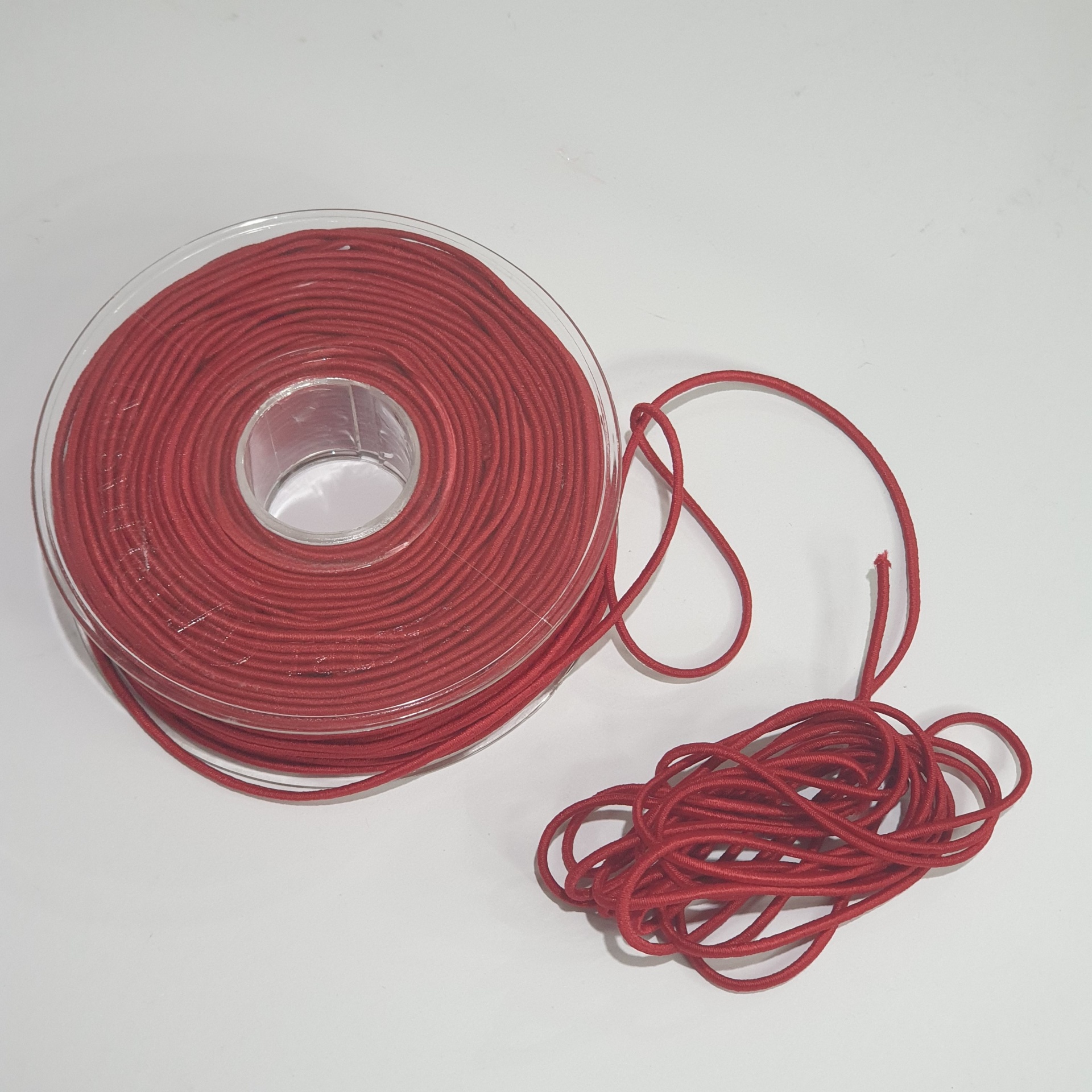Cordão vermelho enrolado em carretel transparente com parte solta em superfície branca