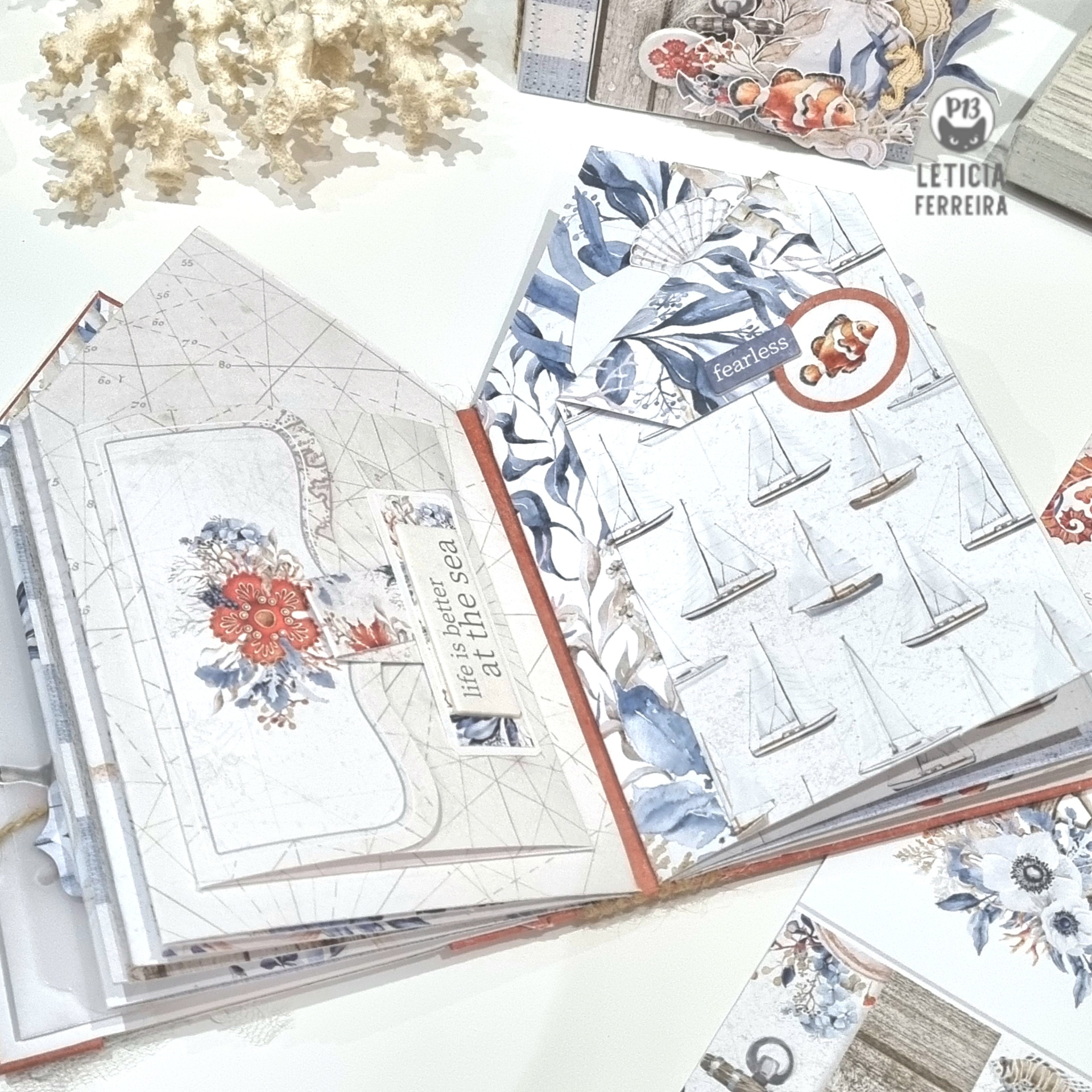 Livro artesanal aberto com páginas decoradas com barcos à vela e flores em azul e vermelho