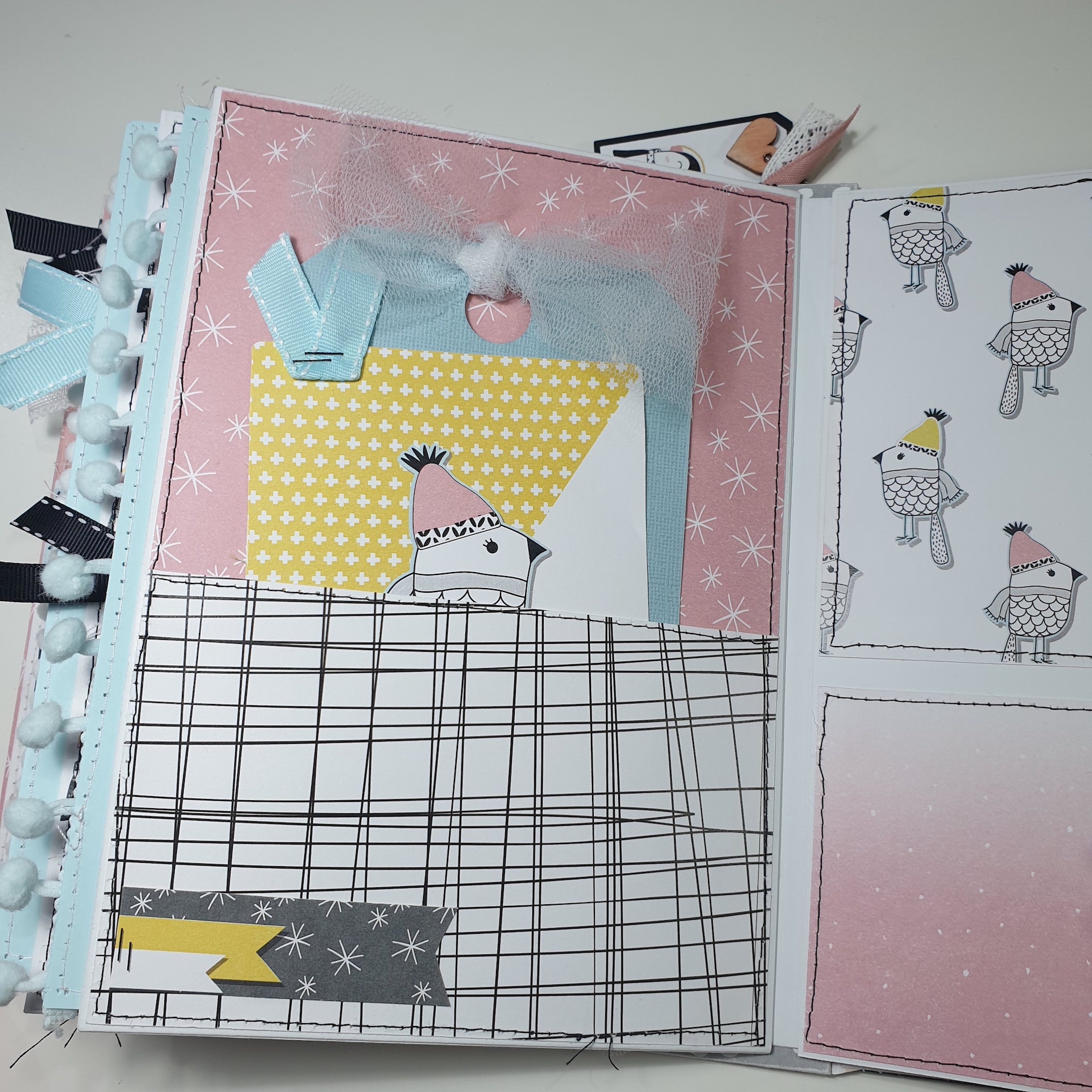 Caderno artesanal com padrões de linhas pretas, estrelas, corações e pássaros, com laços e pompons coloridos