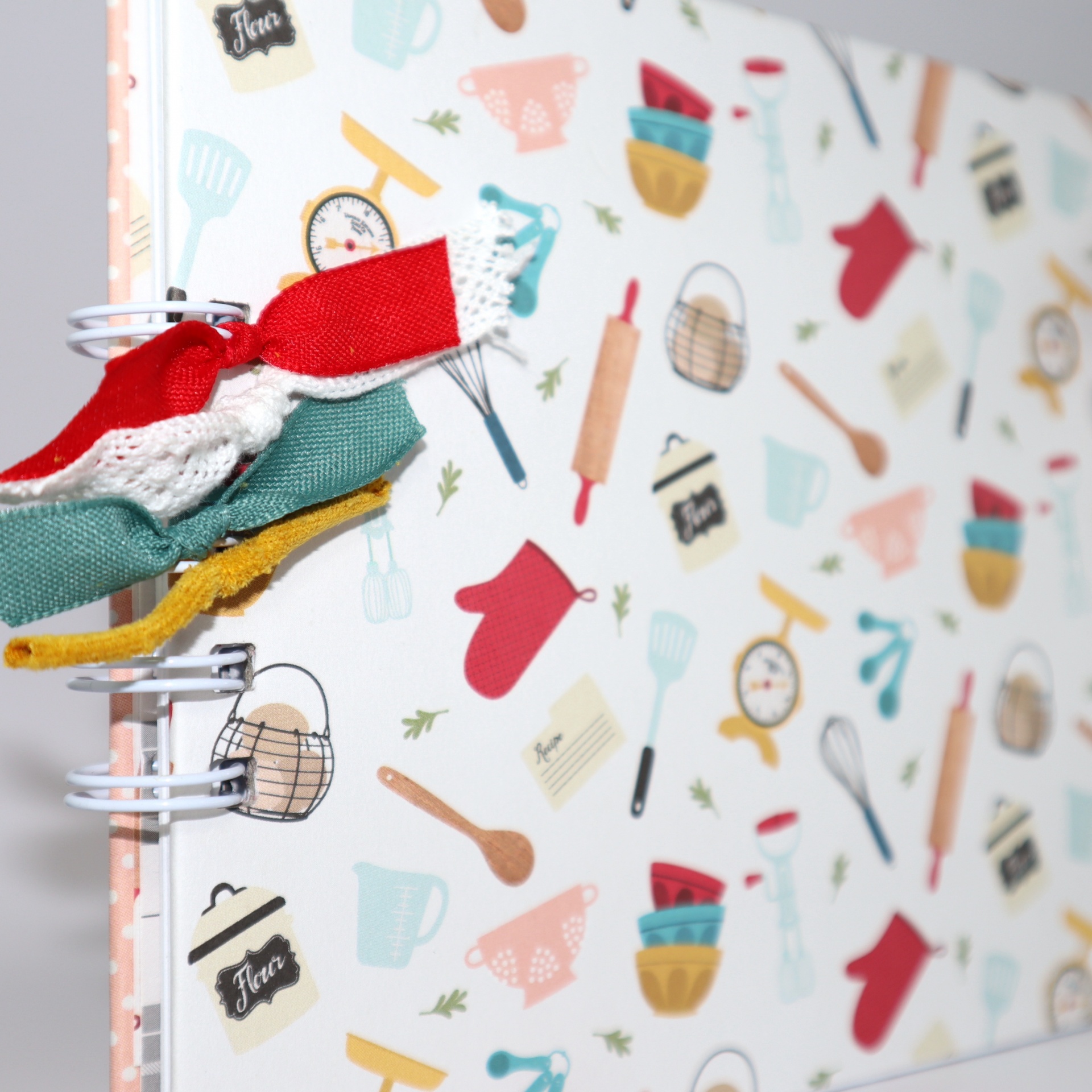 Caderno de receitas com capa decorada por motivos de utensílios de cozinha e fitas coloridas na lombada