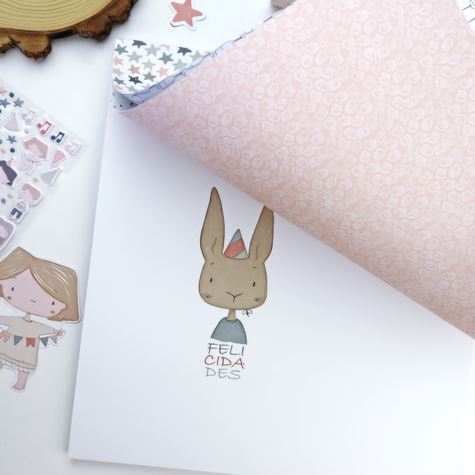 Papel ilustrado com coelho e texto FELICIDADES e papel decorativo rosa com padrão de corações