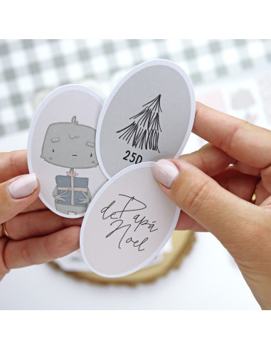 Três etiquetas ovais em papel branco com desenhos e texto seguradas por mãos com unhas pintadas de bege.