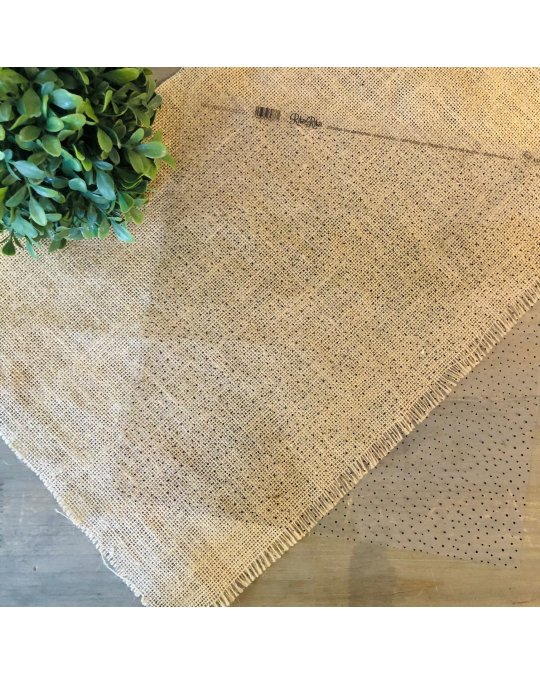 Tecido de juta cru sobre mesa de madeira com padrões pontilhados e ramo verde artificial