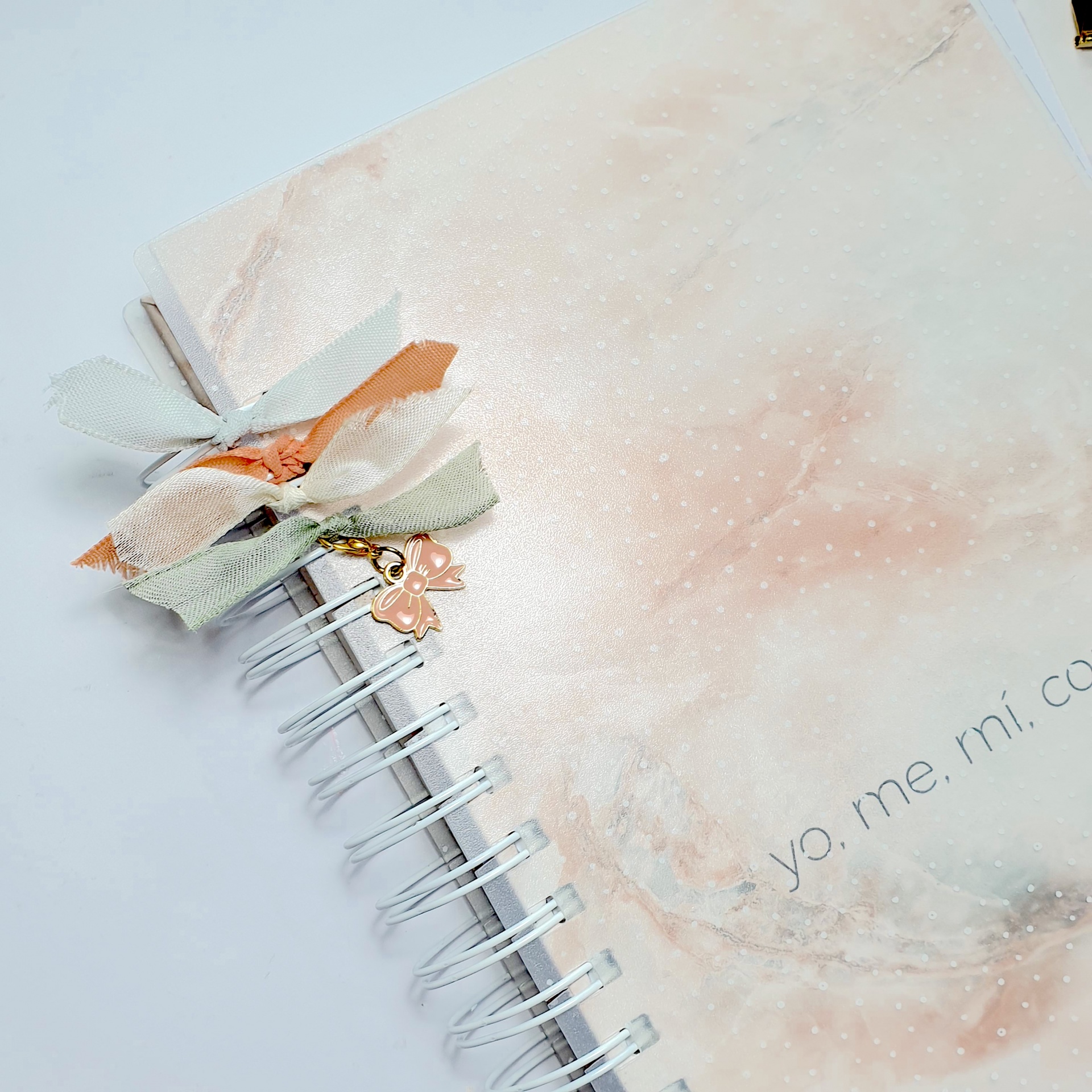 Caderno pastel com capa espiralada e fitas decorativas com pendente