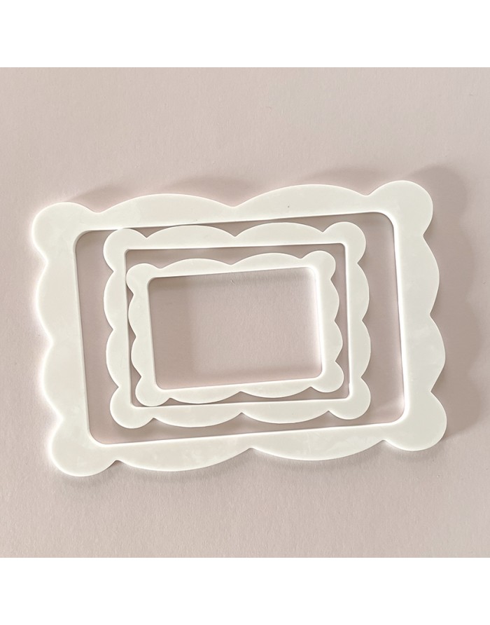 Três moldes de plástico branco com bordas onduladas sobre fundo rosa