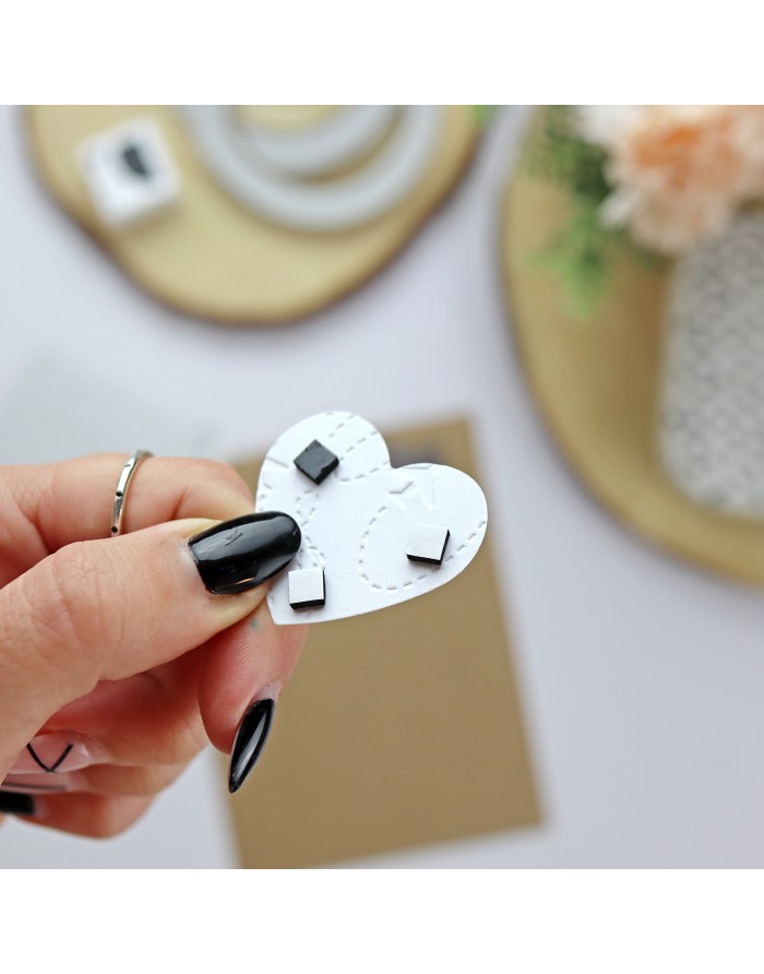 Mão a segurar suporte branco em forma de coração com ímanes pretos