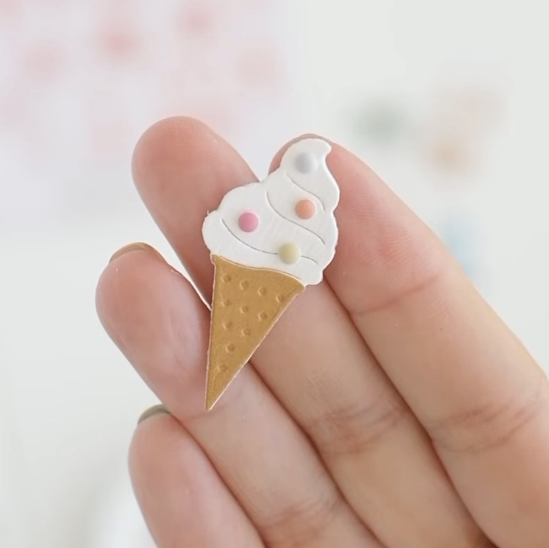 Pequeno adesivo ou pin de gelado com cone castanho e cobertura branca com bolinhas coloridas