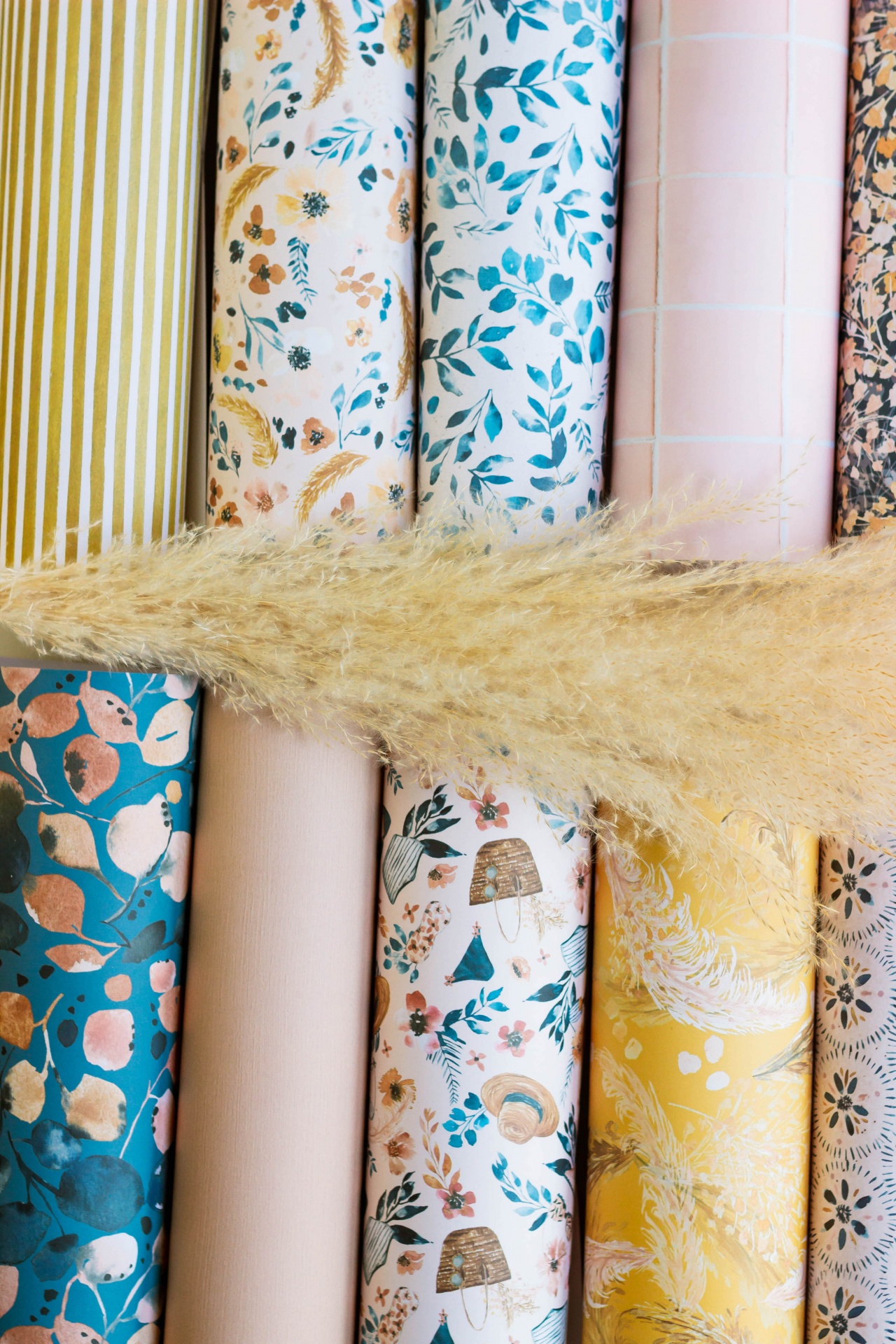 Rolos de papel decorativo com padrões coloridos e um ramo de planta seca por cima