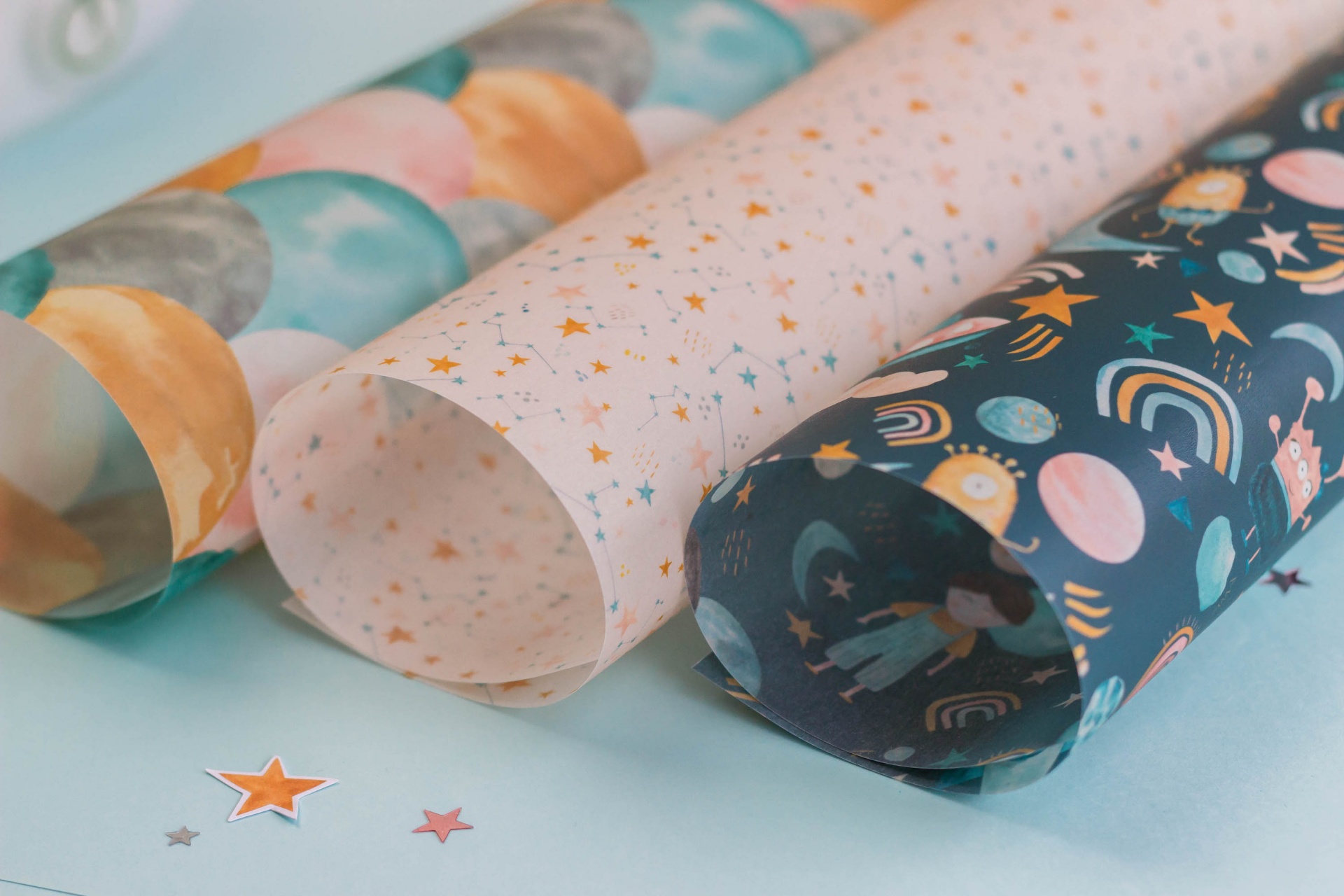 Três rolos de papel de embrulho com padrões coloridos e temas celestes