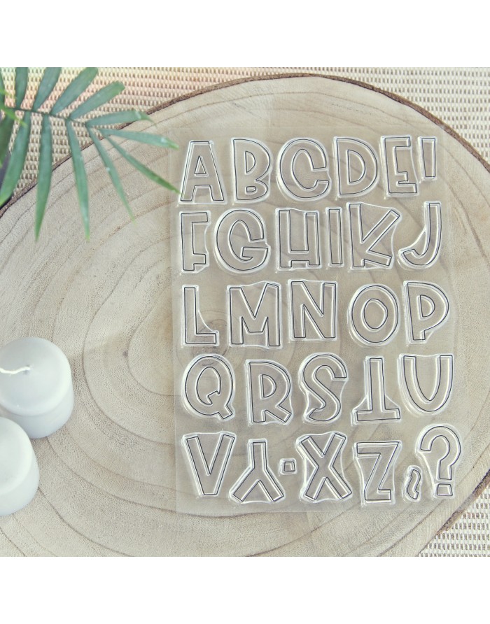 Conjunto de carimbos de letras transparentes sobre base de madeira com velas brancas e folha verde