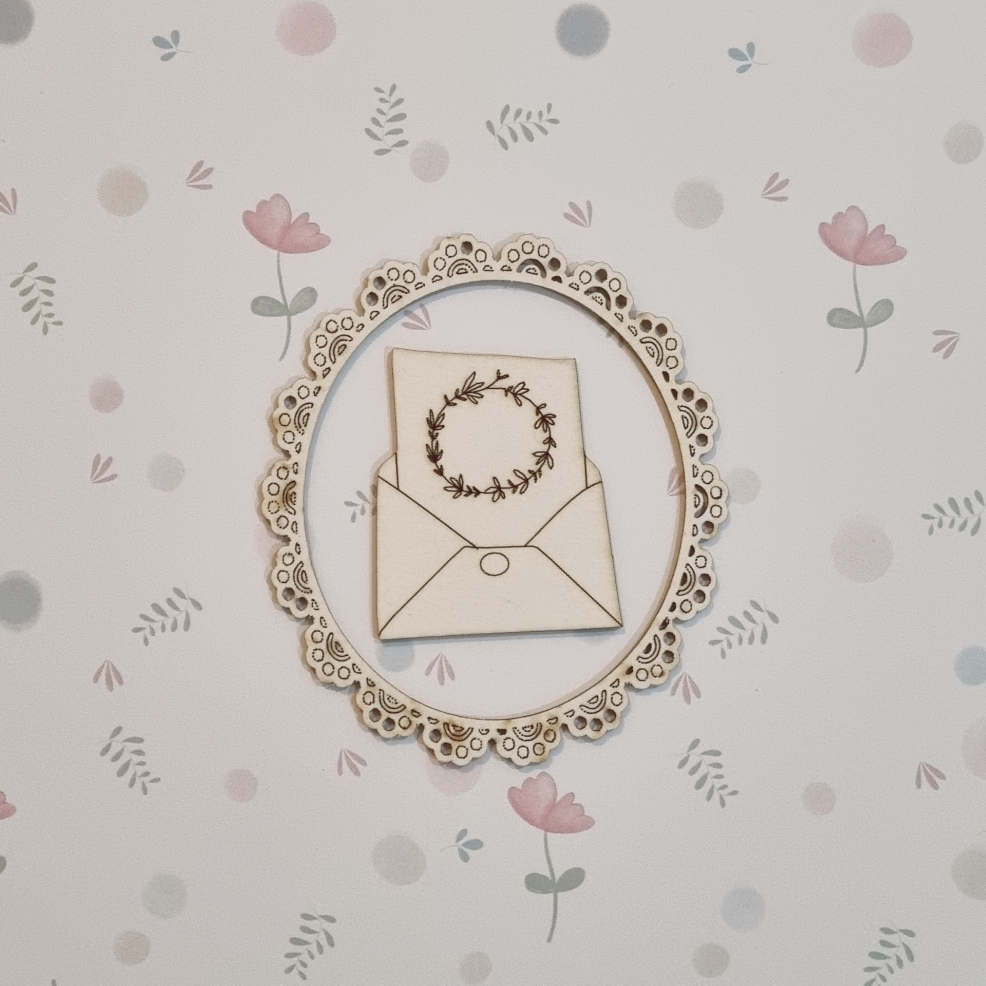 Quadro decorativo com envelope e cartão ilustrado em moldura rendilhada sobre papel de parede floral