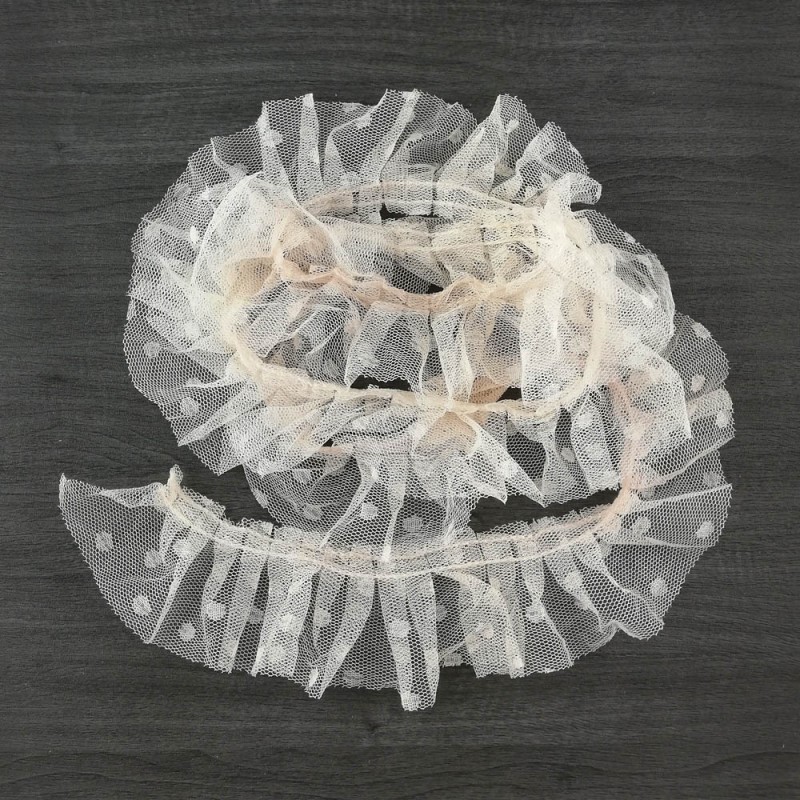 Fita decorativa de tule branco com bolinhas sobre fundo de madeira escura