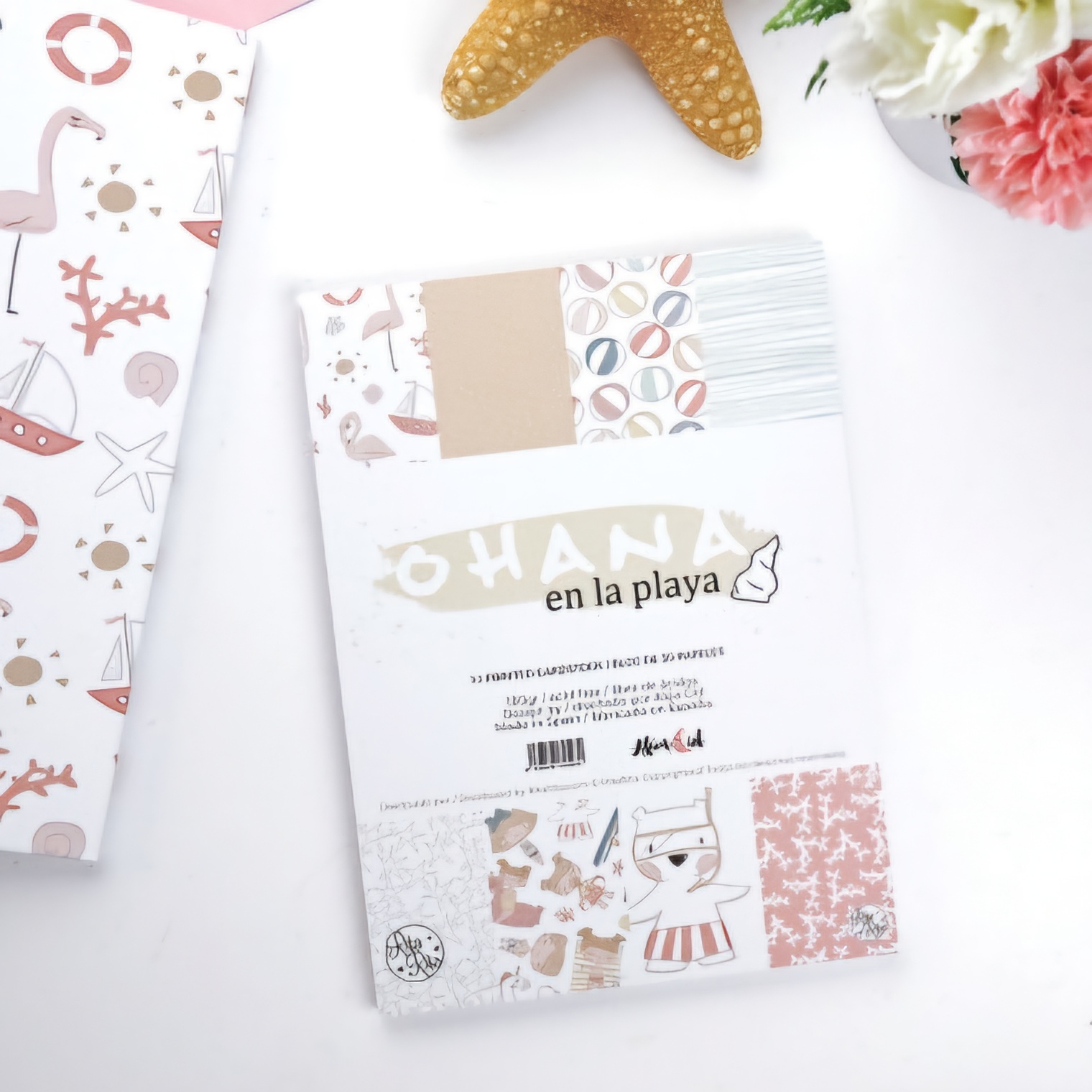 Bloco de papel decorativo com padrões temáticos de praia, em cores bege, azul, laranja e rosa, sobre fundo branco com decoração de estrela-do-mar e flores.