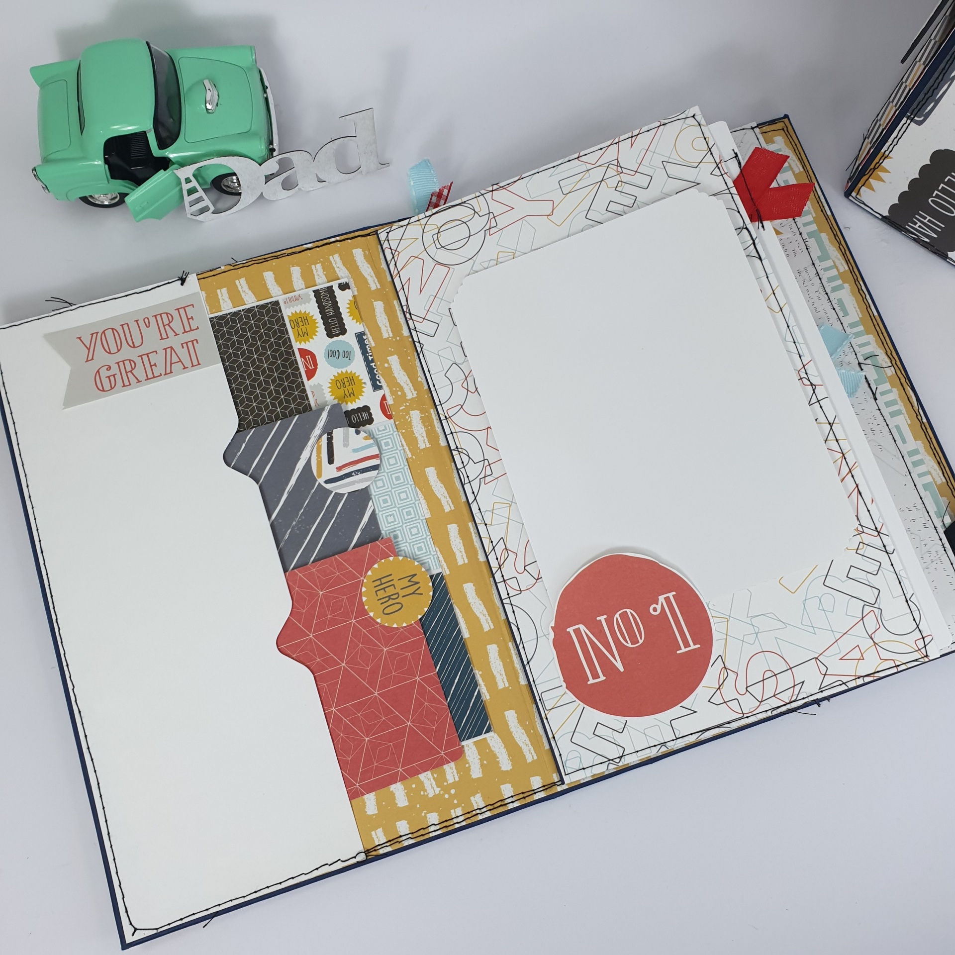 Livro de scrapbook aberto com páginas decoradas coloridas e carro de brinquedo verde ao lado