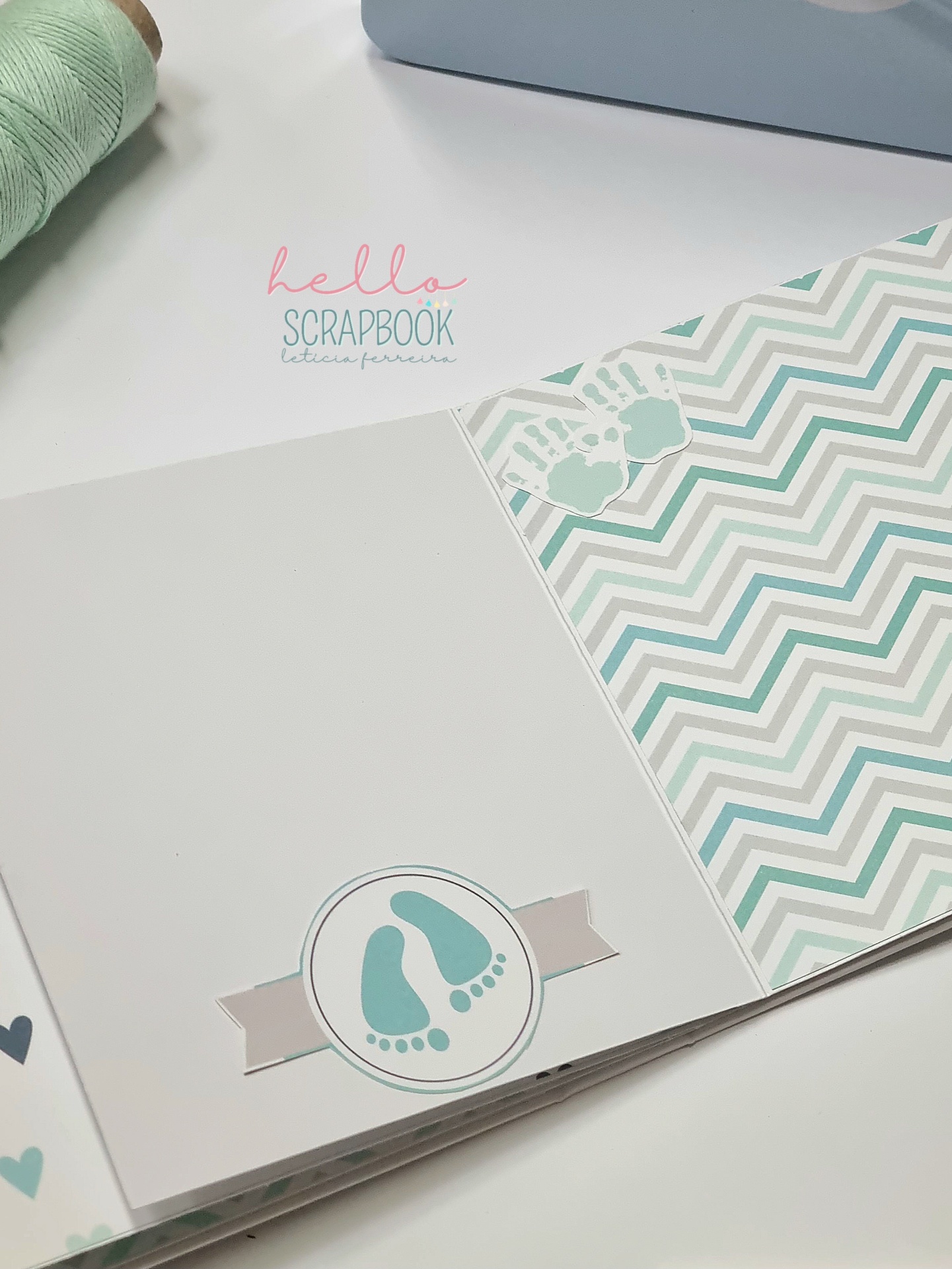 Página de scrapbook com padrões geométricos e pegadas de bebé azuis sobre fundo branco