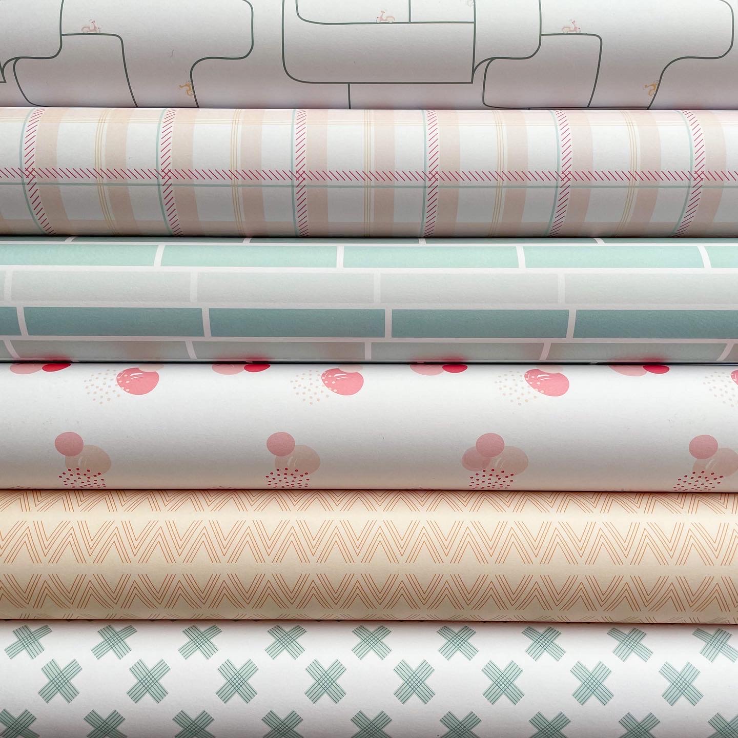 Rolos de papel decorativo com padrões geométricos e de pontos em tons pastel sobre fundo branco