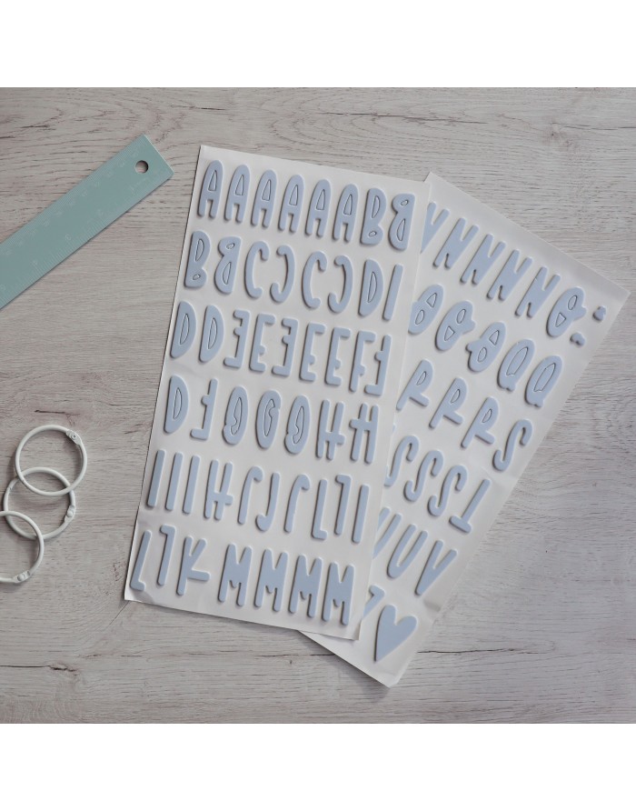 Dois conjuntos de autocolantes de letras maiúsculas em branco com borda cinza sobre superfície de madeira clara