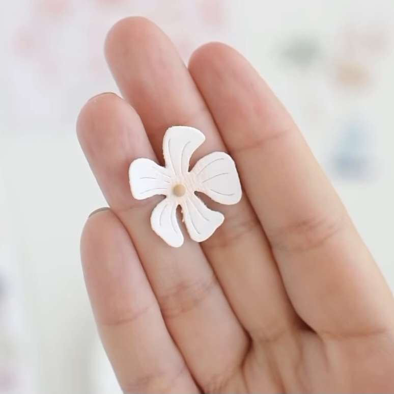 Flor branca pequena com cinco pétalas arredondadas entre os dedos de uma mão.