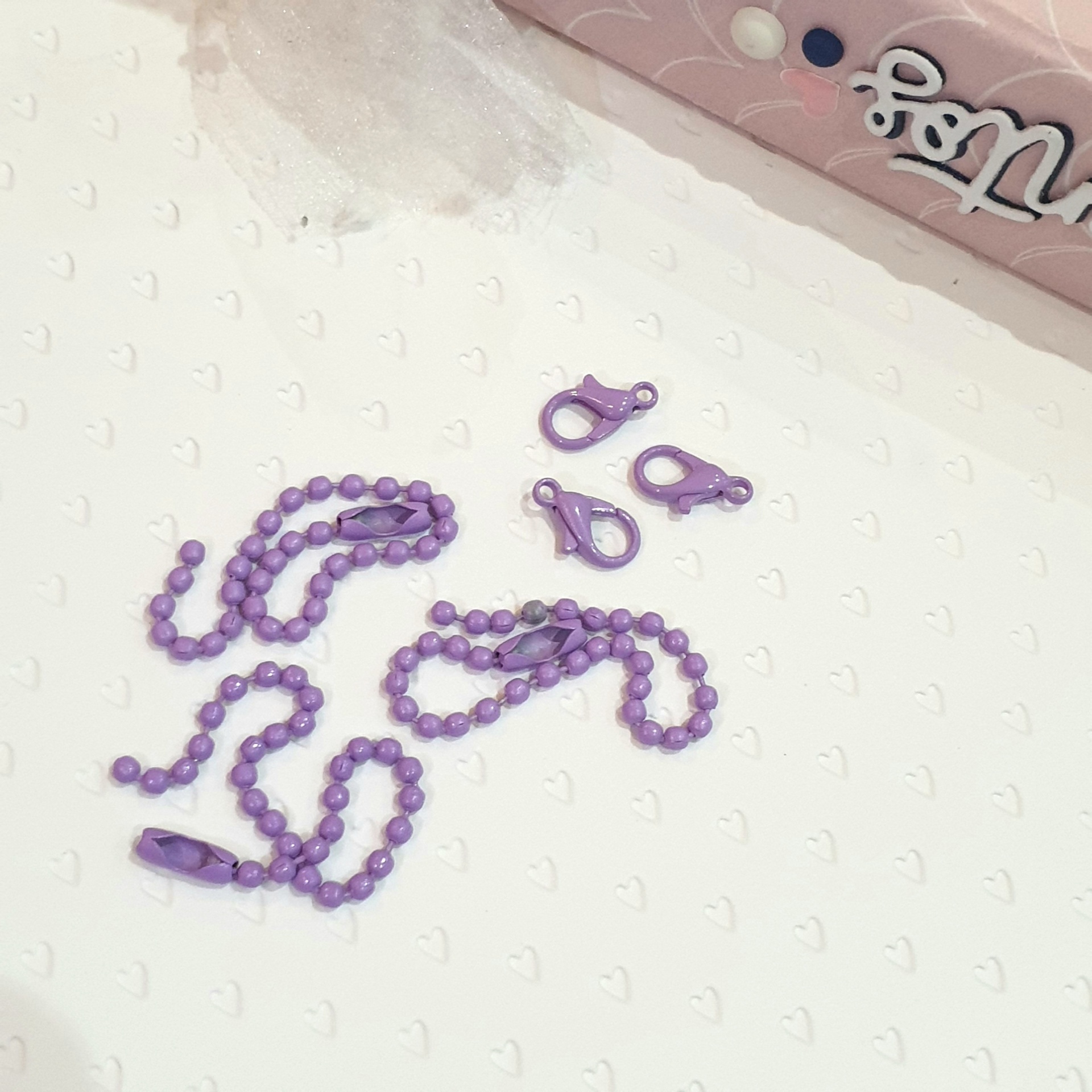 Conjunto de correntes lilás com fechos sobre fundo branco texturizado com corações