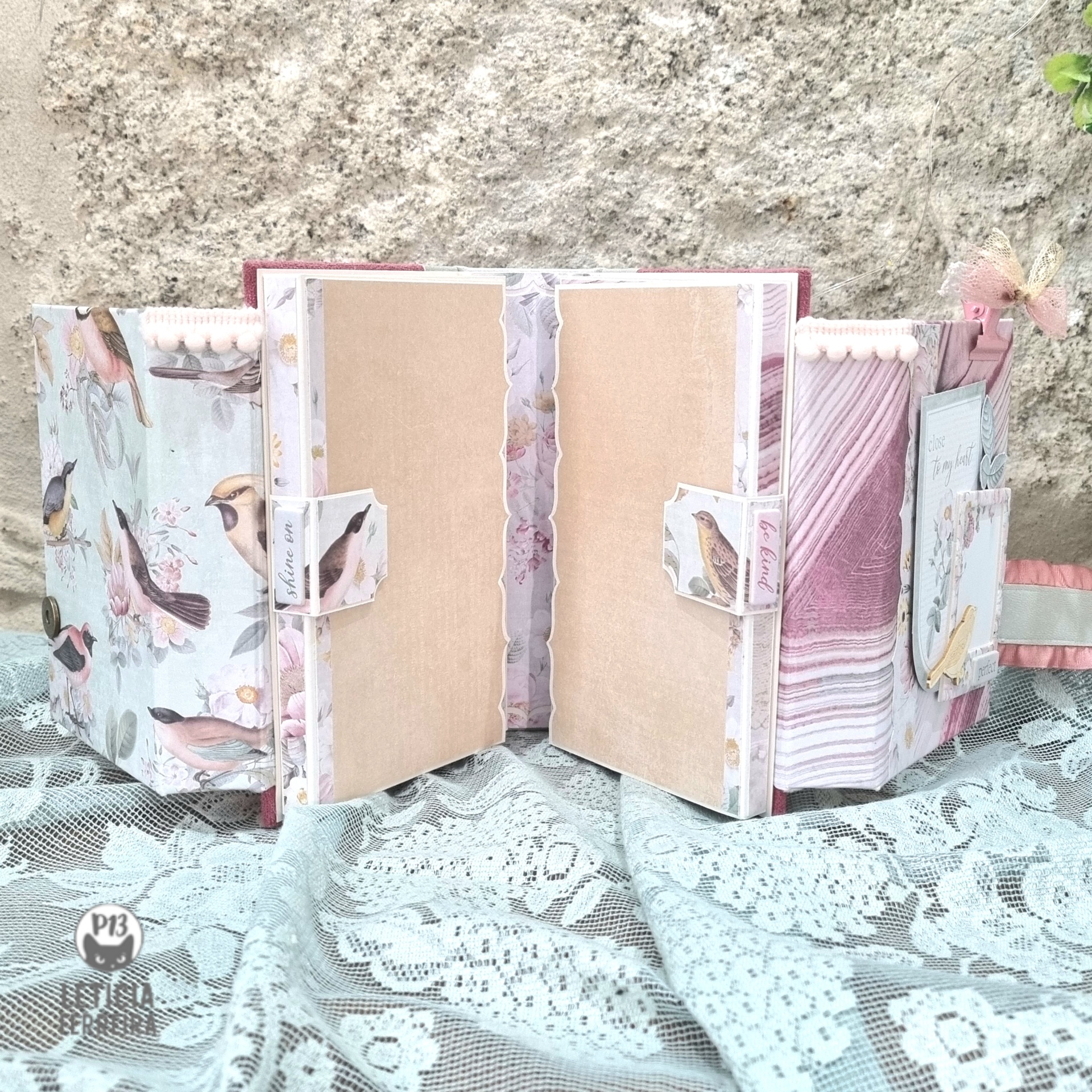 Álbum decorado em tons pastel com motivos de pássaros e flores sobre renda branca
