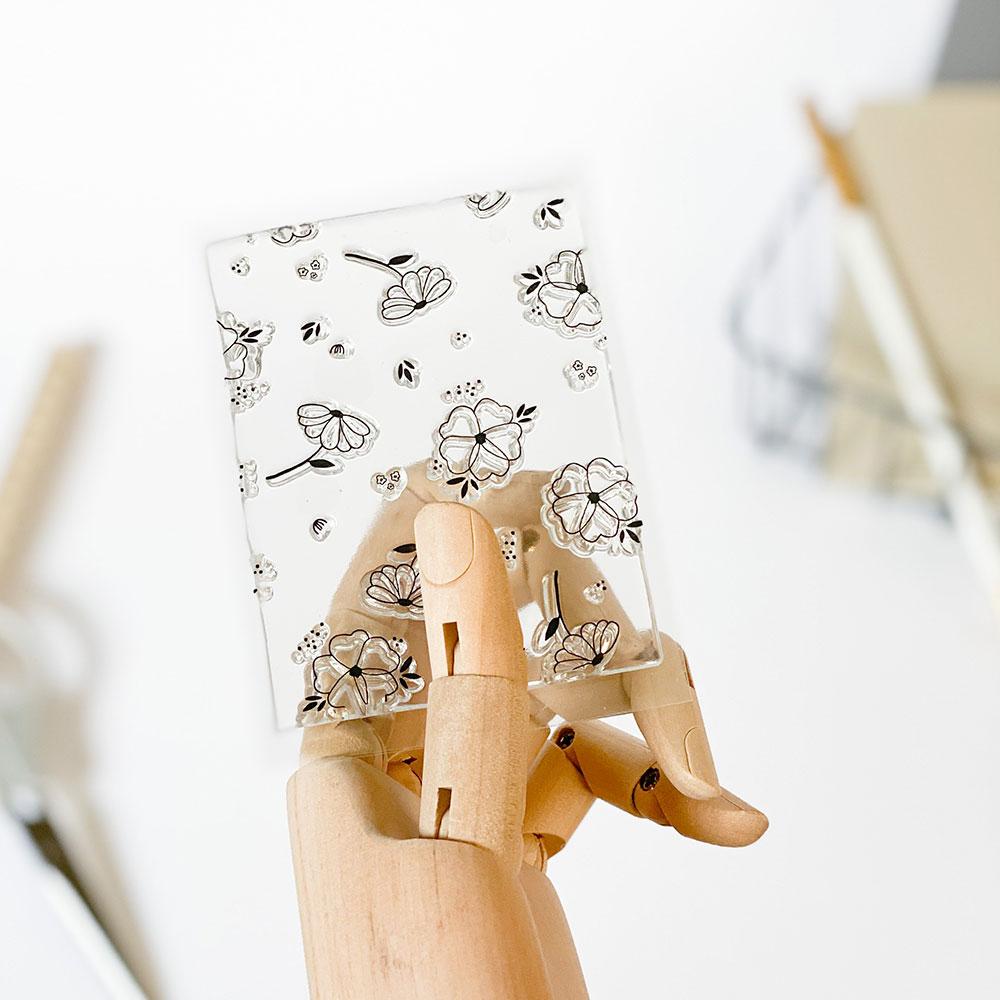 Mão de manequim de madeira segurando cartão floral e borboletas preto sobre branco