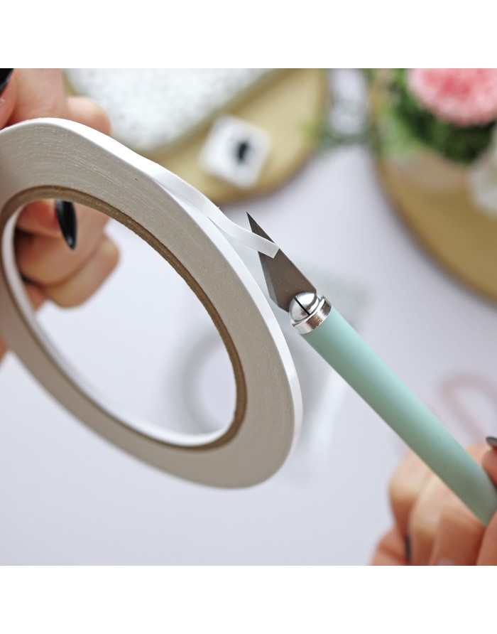 Rolo de fita dupla face sendo cortado com estilete de cabo verde