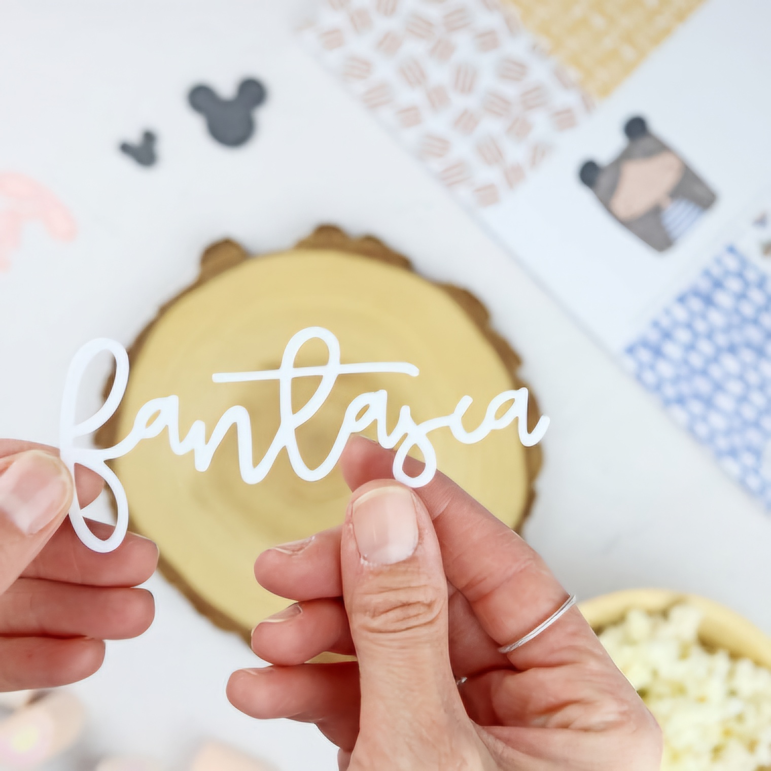 Recorte branco com palavra 'fantasia' em mãos sobre fundo claro com madeira e pipocas