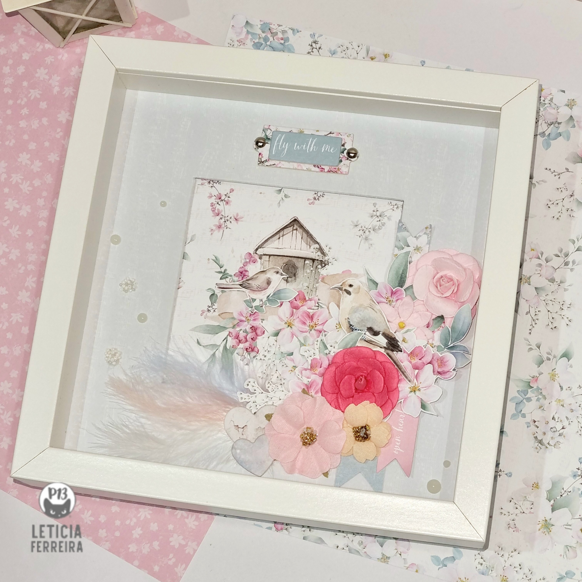 Quadro decorativo branco com flores e pássaro em relevo sobre mesa rosa e floral