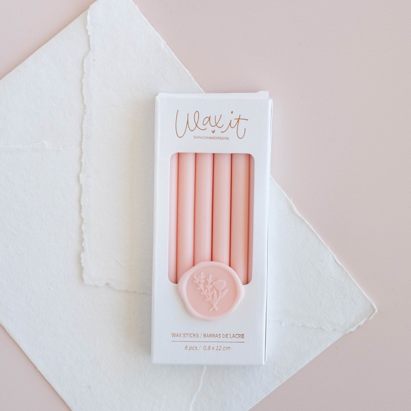 Conjunto de velas cor-de-rosa em embalagem branca com selo rosa decorativo em fundo rosa claro