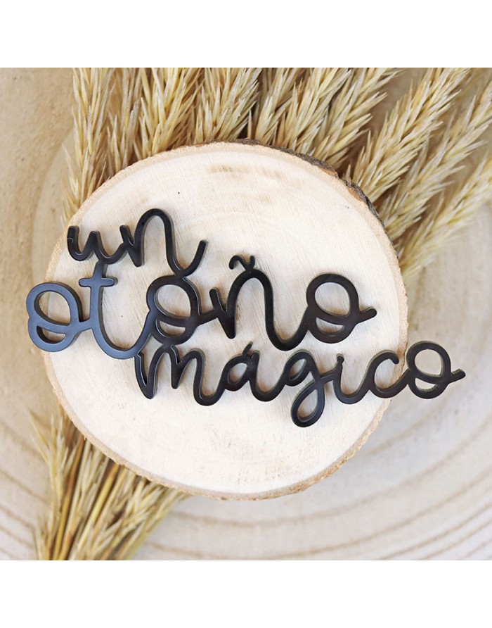 Adorno metálico preto com a frase 'un otoño mágico' sobre base de madeira e plantas secas