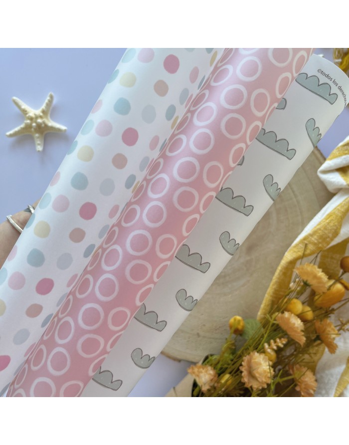 Três rolos de papel decorativo em tons pastel com padrões variados colocados em superfície clara