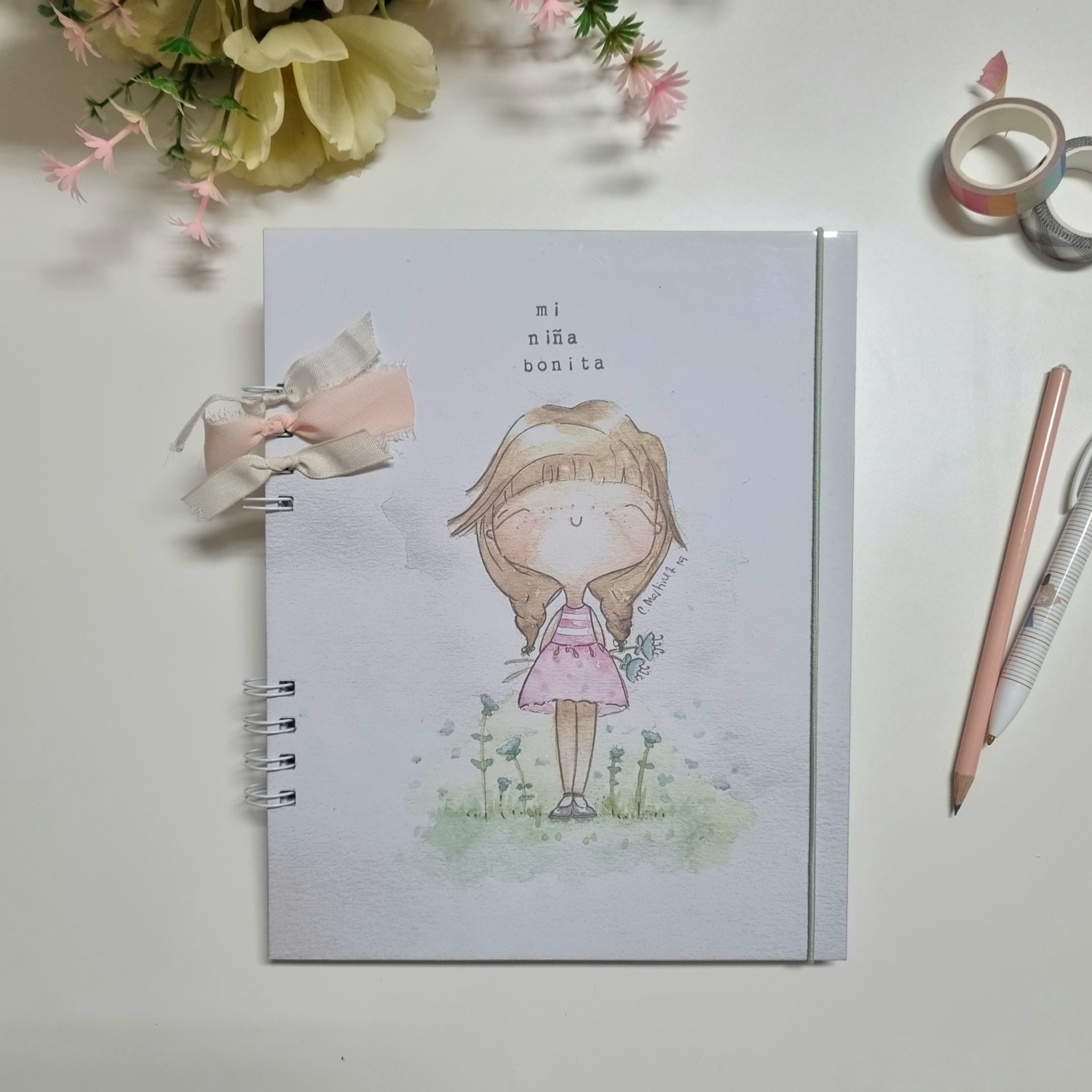 Caderno branco com ilustração de menina loira e texto 'mi niña bonita'