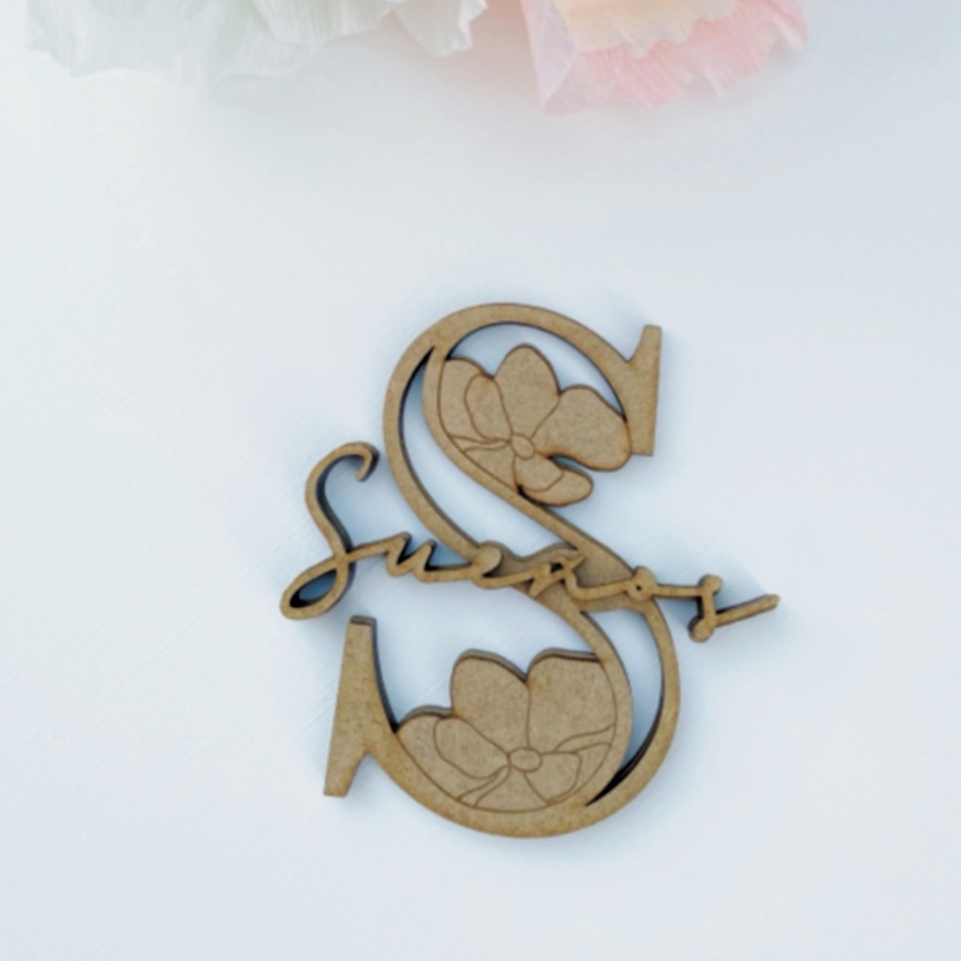 Peça decorativa em madeira clara em forma da letra S com flores recortadas e palavra 'smart'