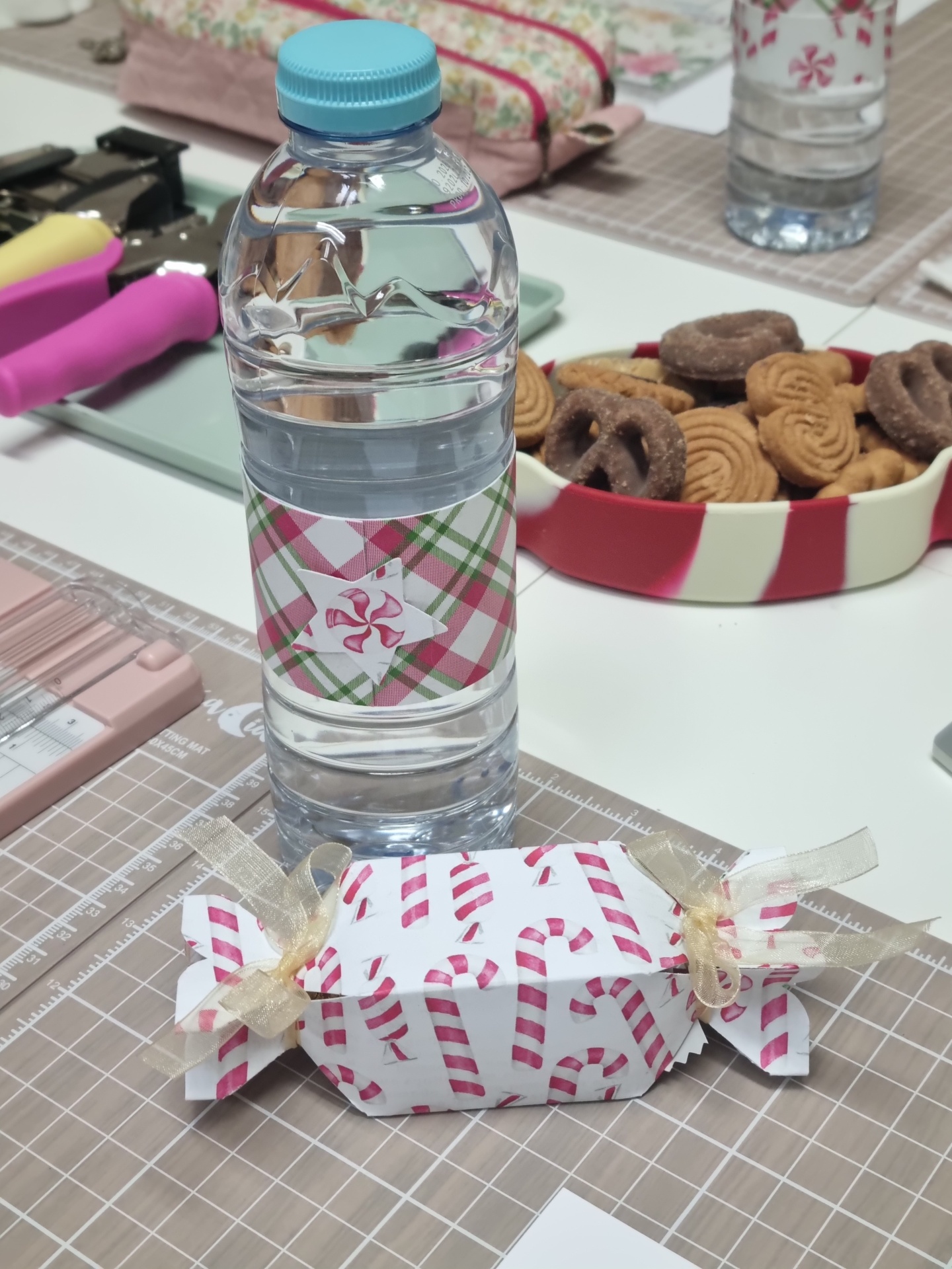 Garrafa de água decorada e caixa de presente com padrão de bengalas de doces vermelhas sobre mesa