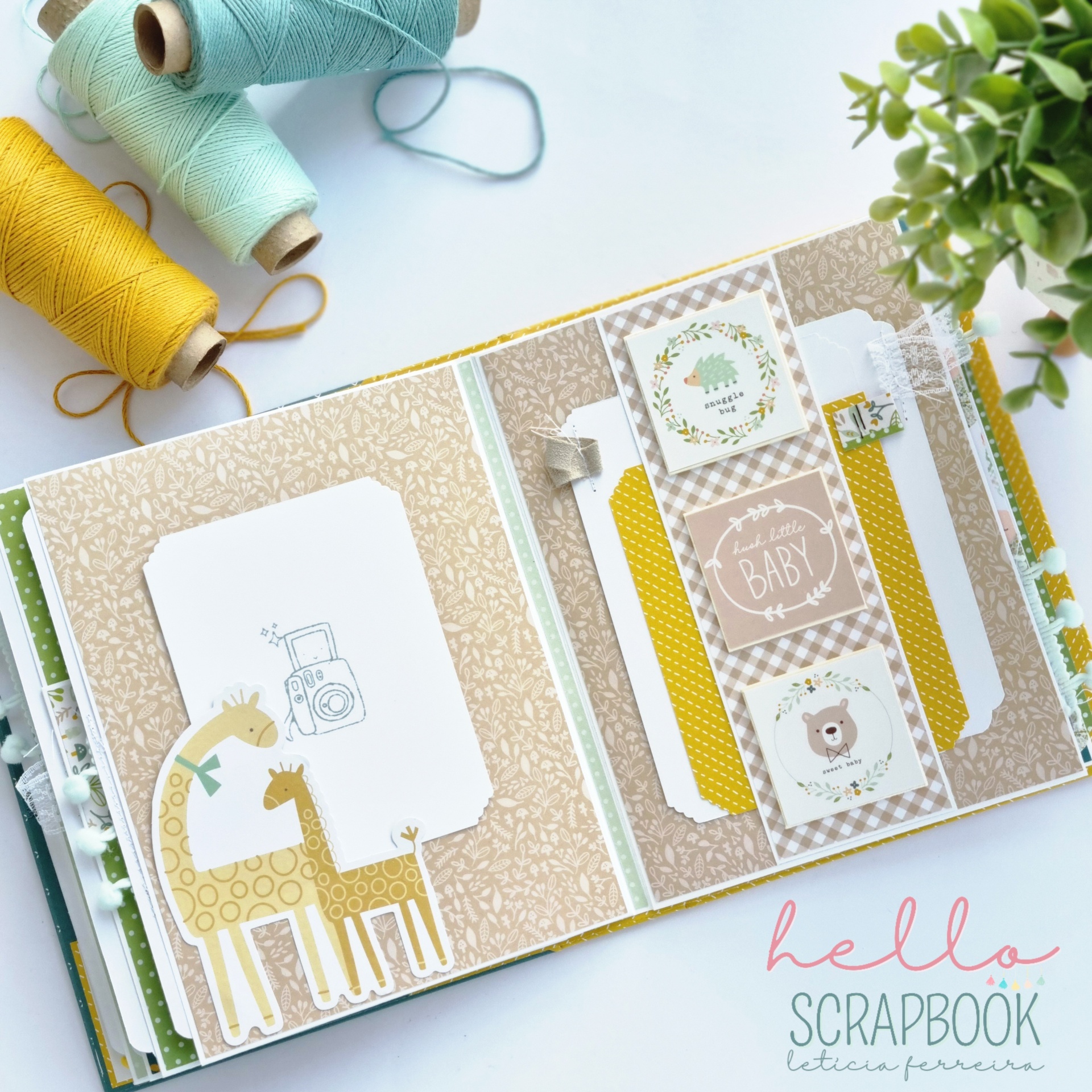 Álbum scrapbook decorado com desenhos de girafas, ursinho e máquina fotográfica, com etiquetas de texto, entre carretéis de linha e planta