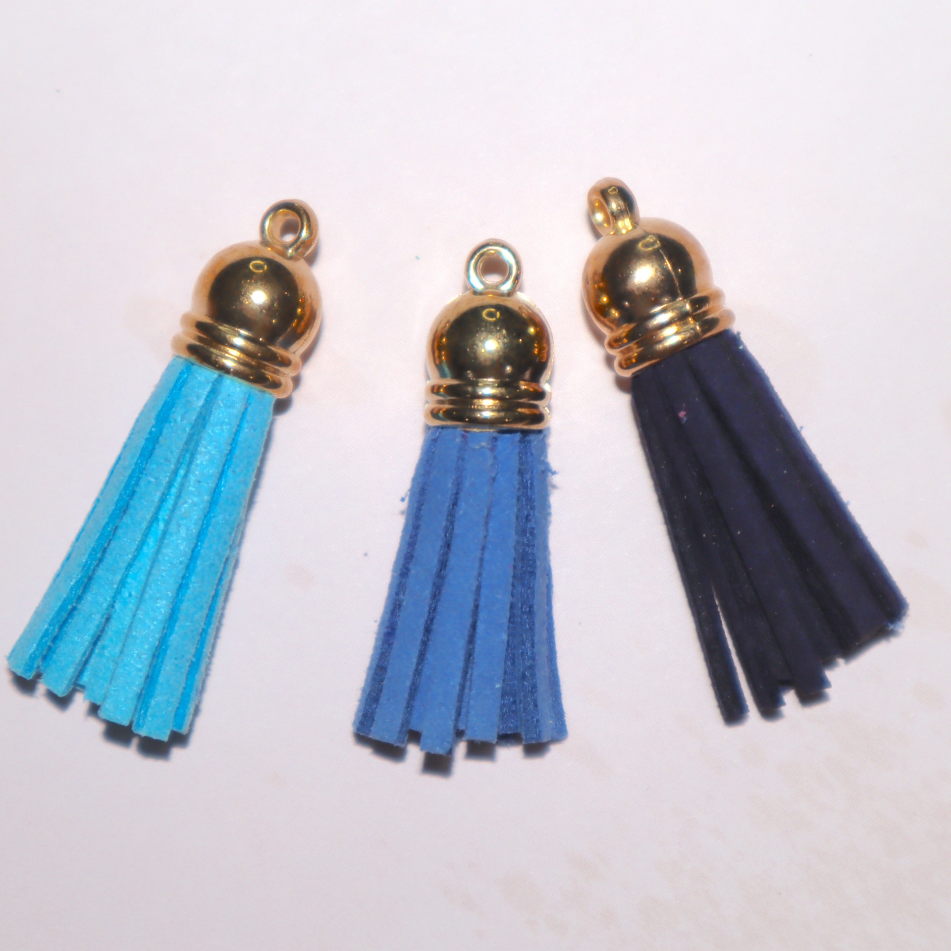 Três tassels de camurça azul turquesa, azul royal e preto com topo dourado sobre fundo branco